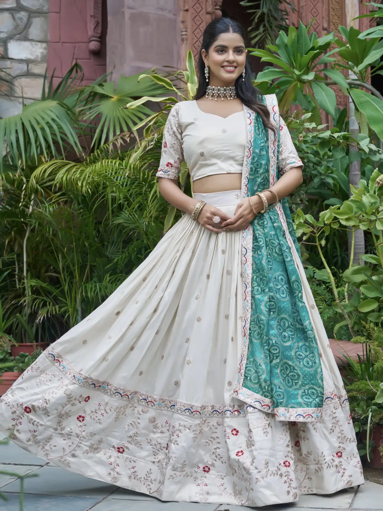 Woman in a traditional outfit with a white blouse and green dupatta standing in a garden.