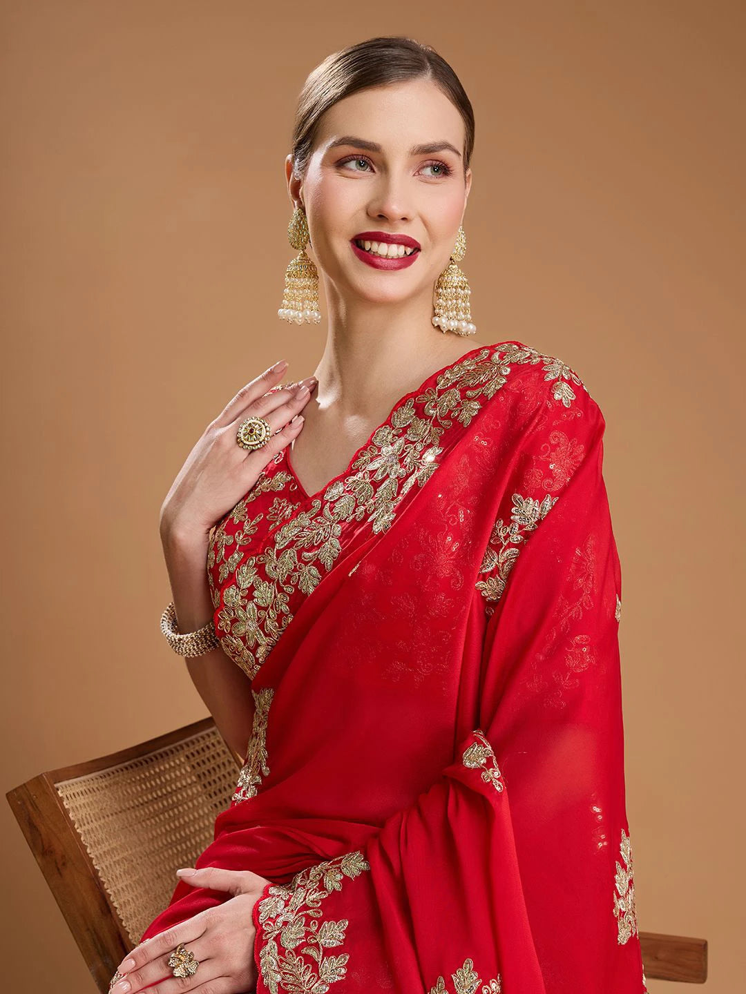 Woman wearing a red saree with gold embroidery on a brown background