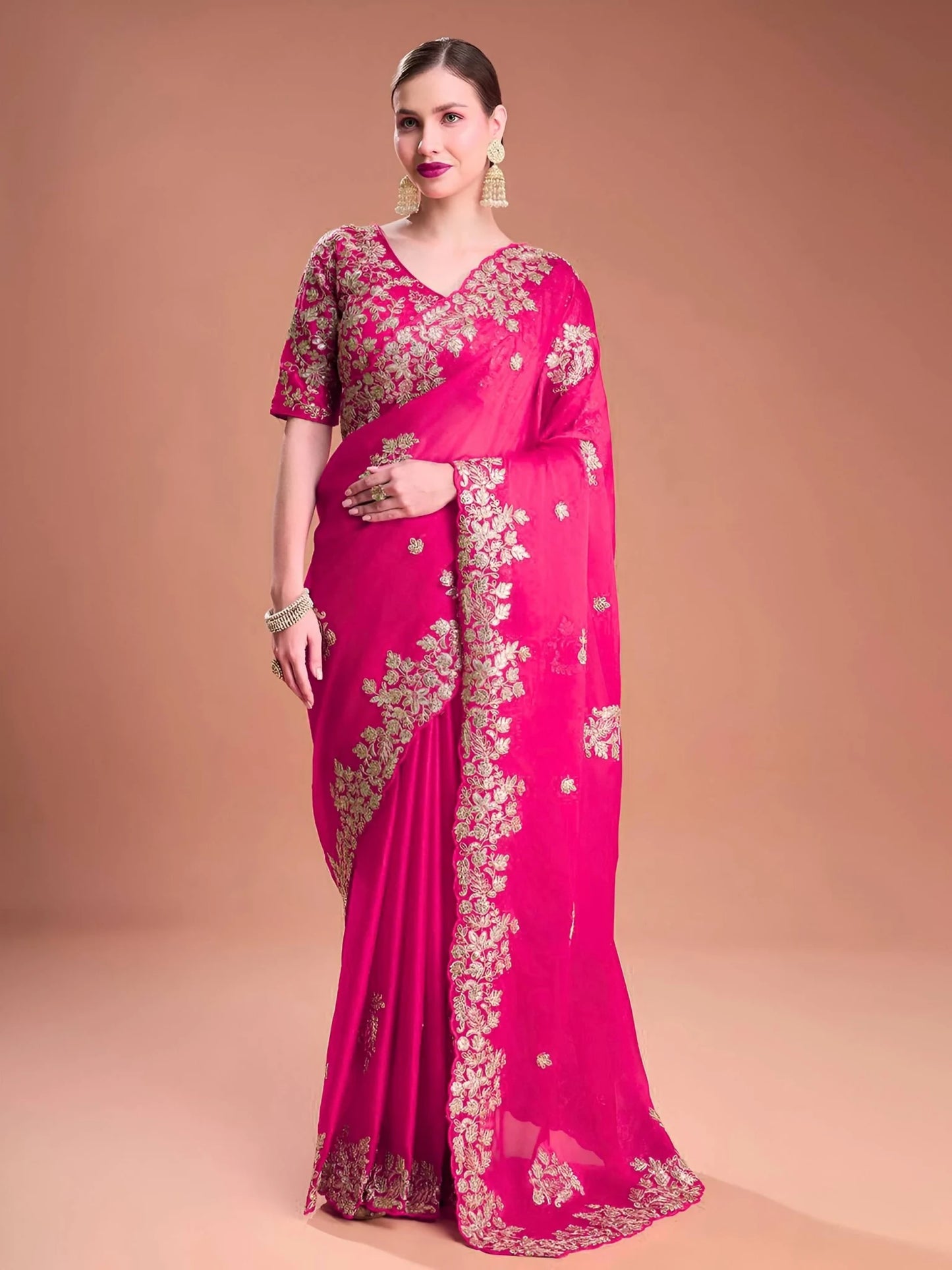 Woman wearing a pink saree with gold embroidery on a beige background