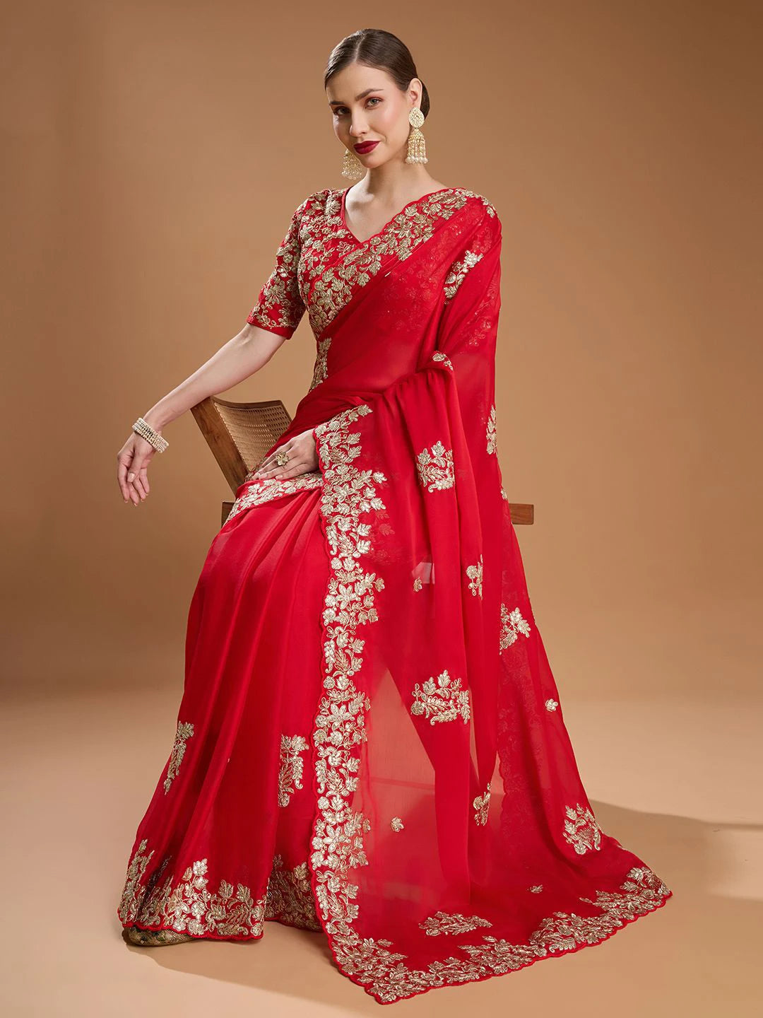 Red saree with gold embroidery on a model against a beige background