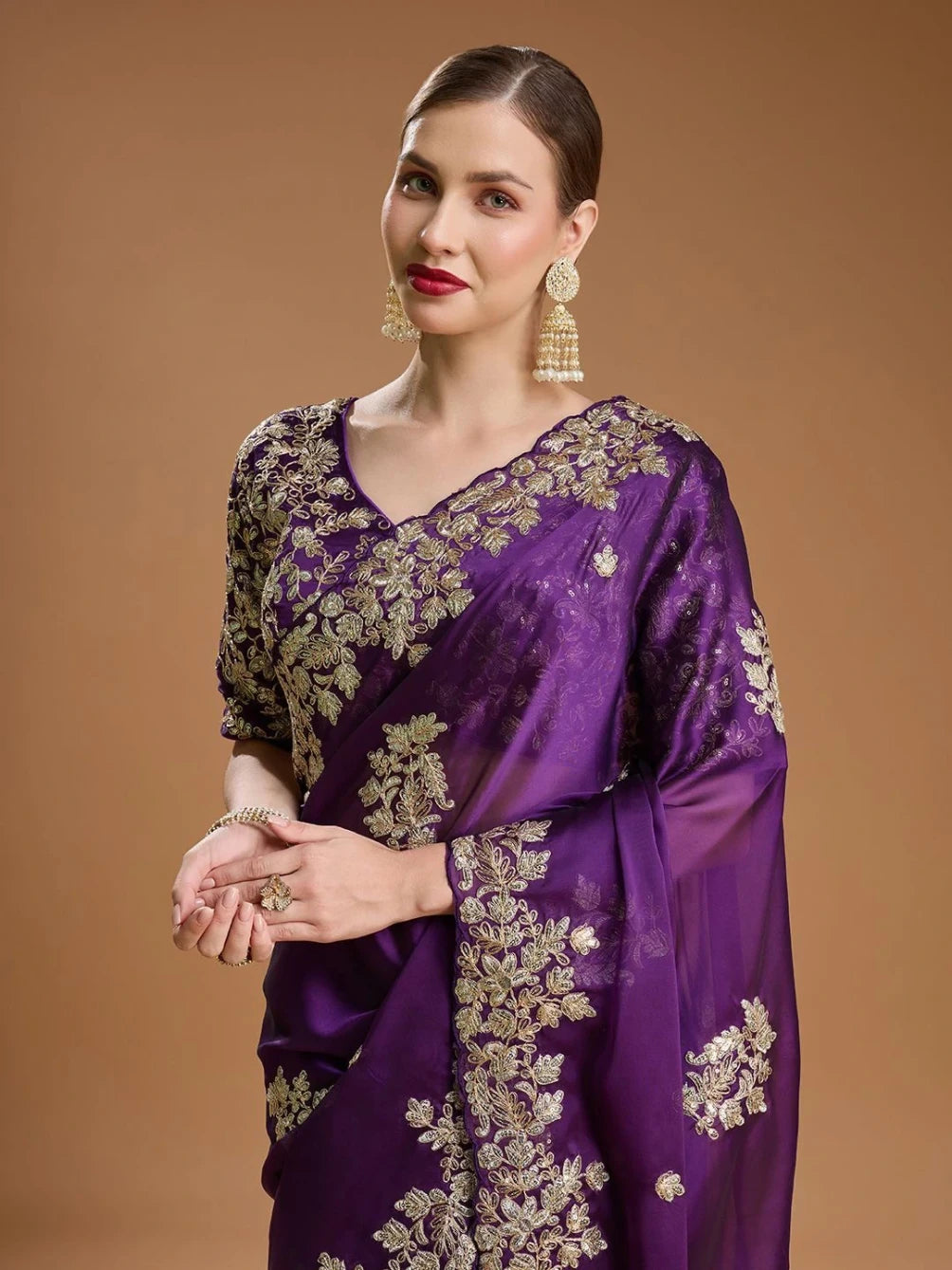 Woman wearing a purple saree with gold embroidery on a brown background