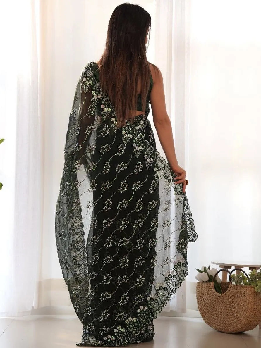Woman wearing a black floral dress with sheer overlay in a bright room.