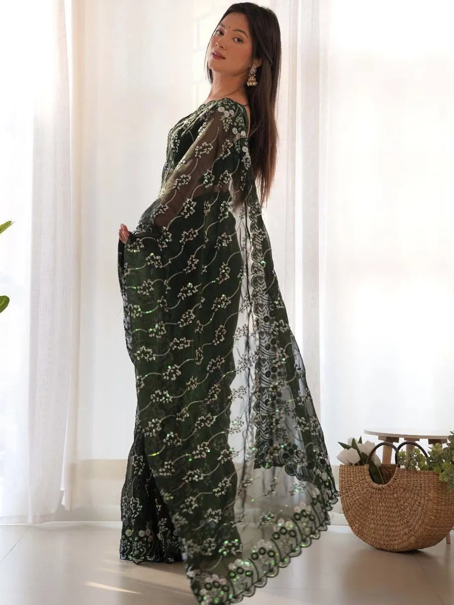 Woman wearing a dark green saree with white patterns in a bright room.