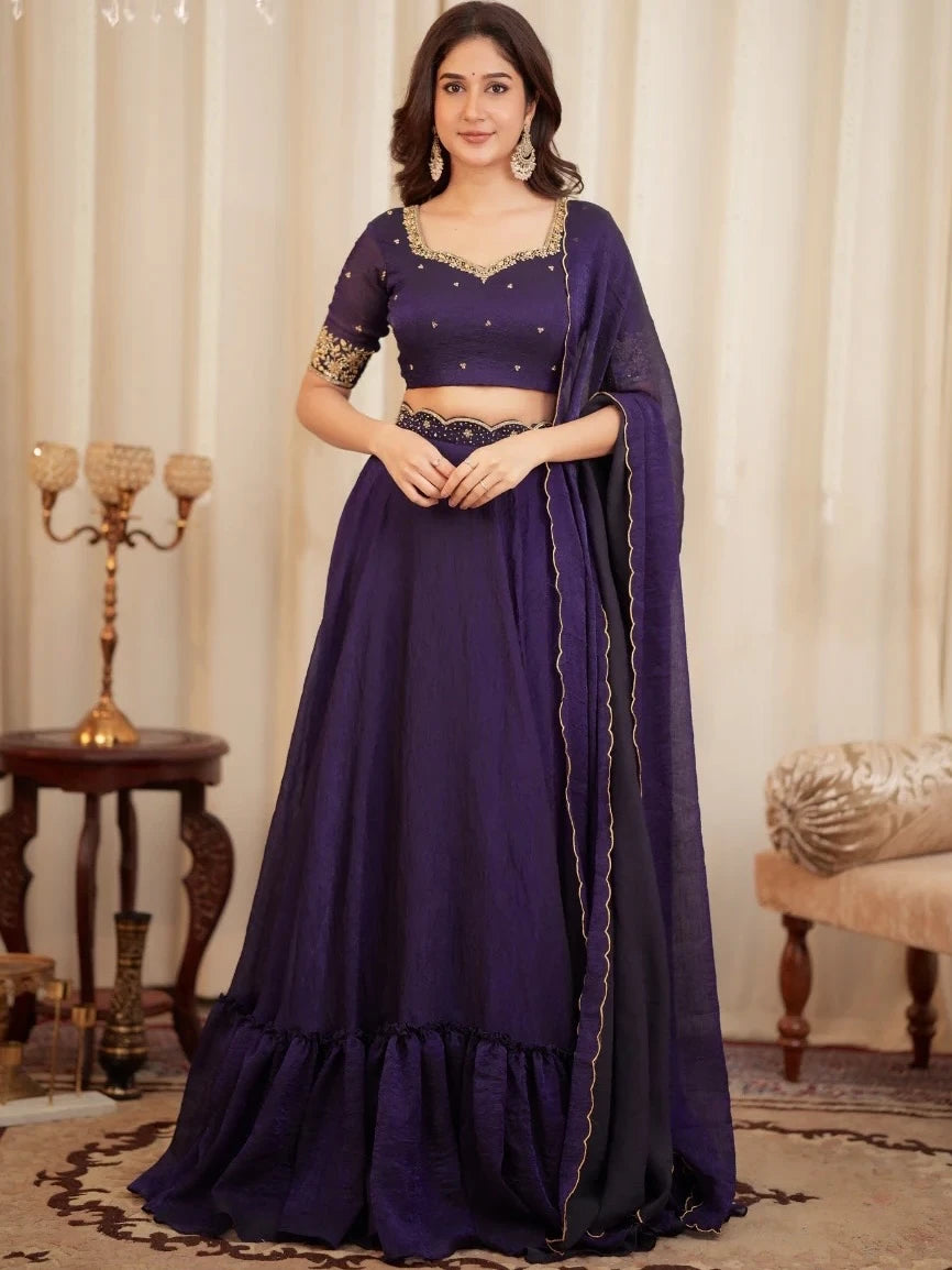 Woman wearing a purple traditional outfit with gold details in a decorated room.