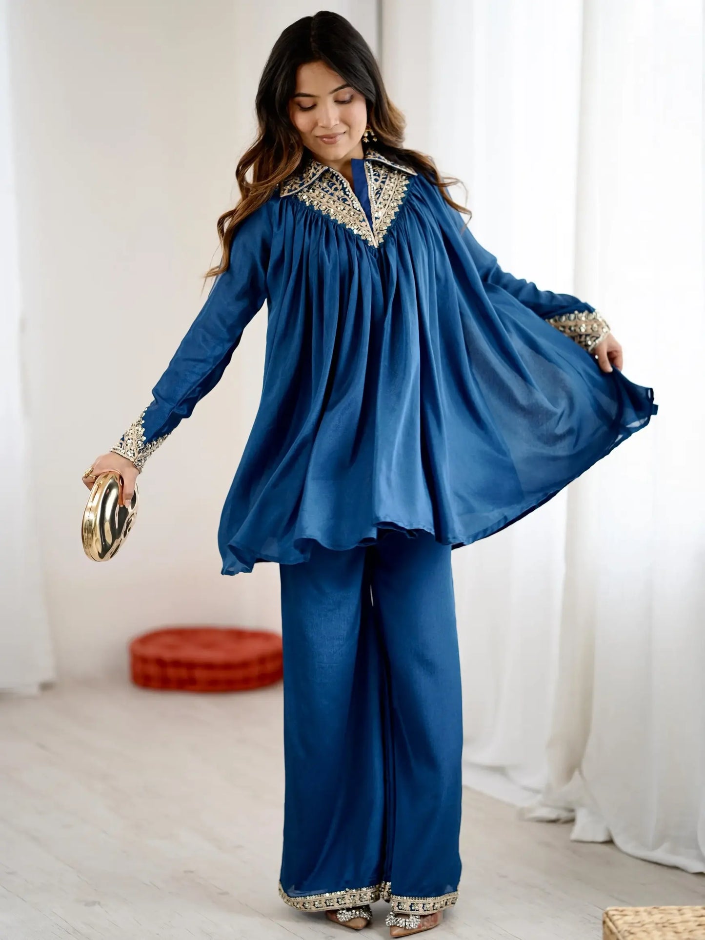 Woman wearing a blue traditional outfit with gold embroidery in a bright room.