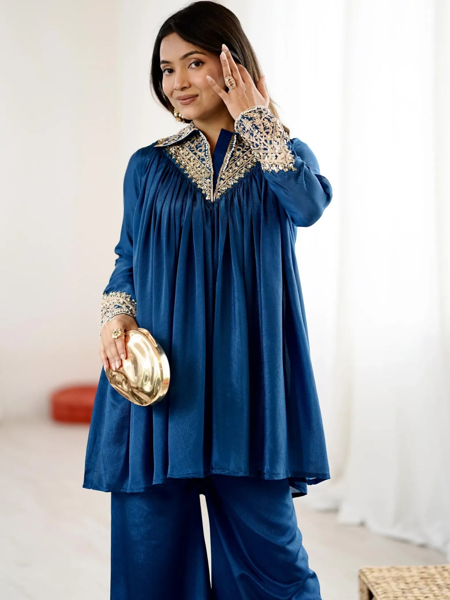 Woman wearing a blue outfit with intricate detailing, holding a gold clutch.