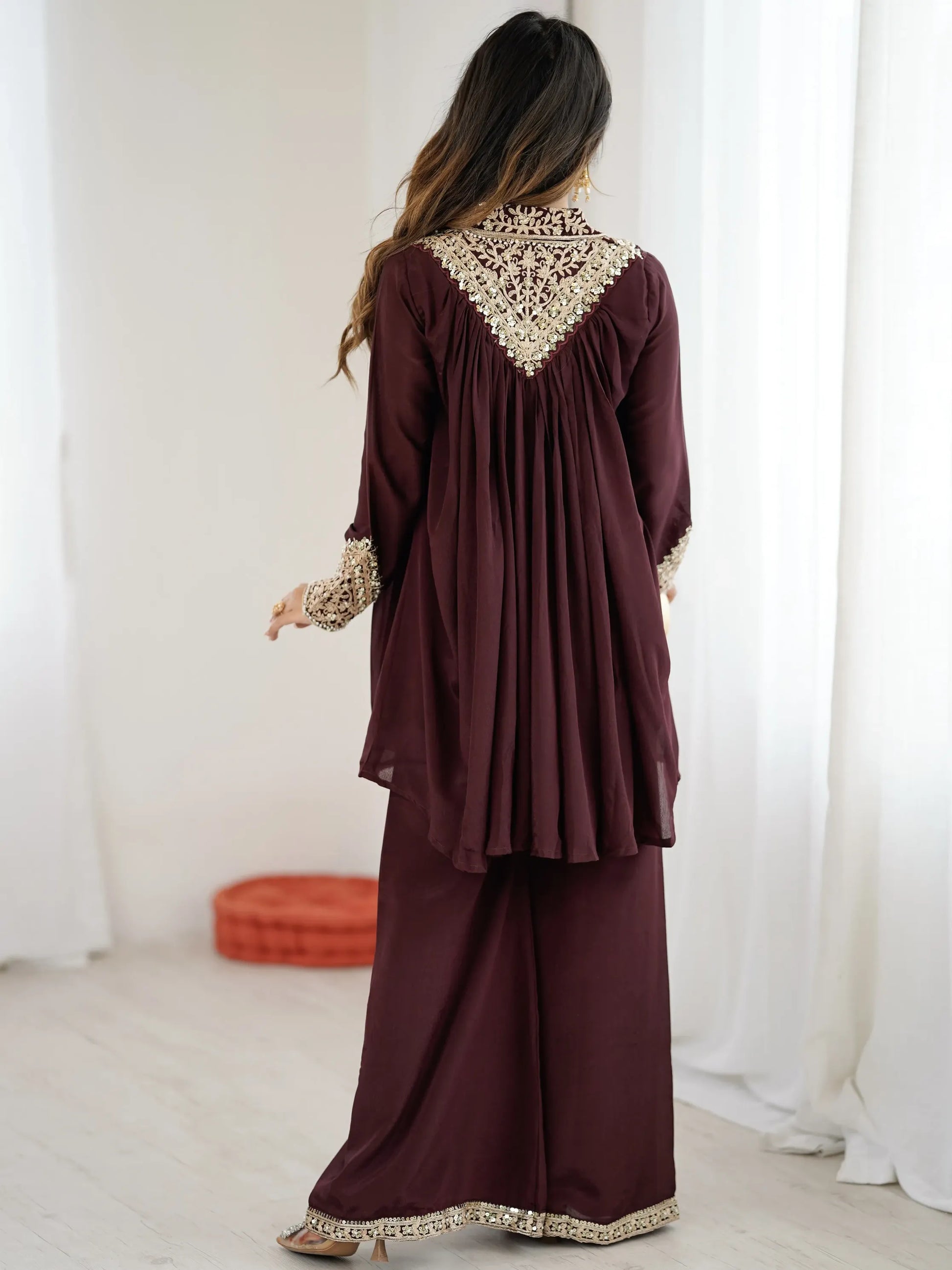 Woman wearing a burgundy dress with gold embroidery in a minimalistic setting
