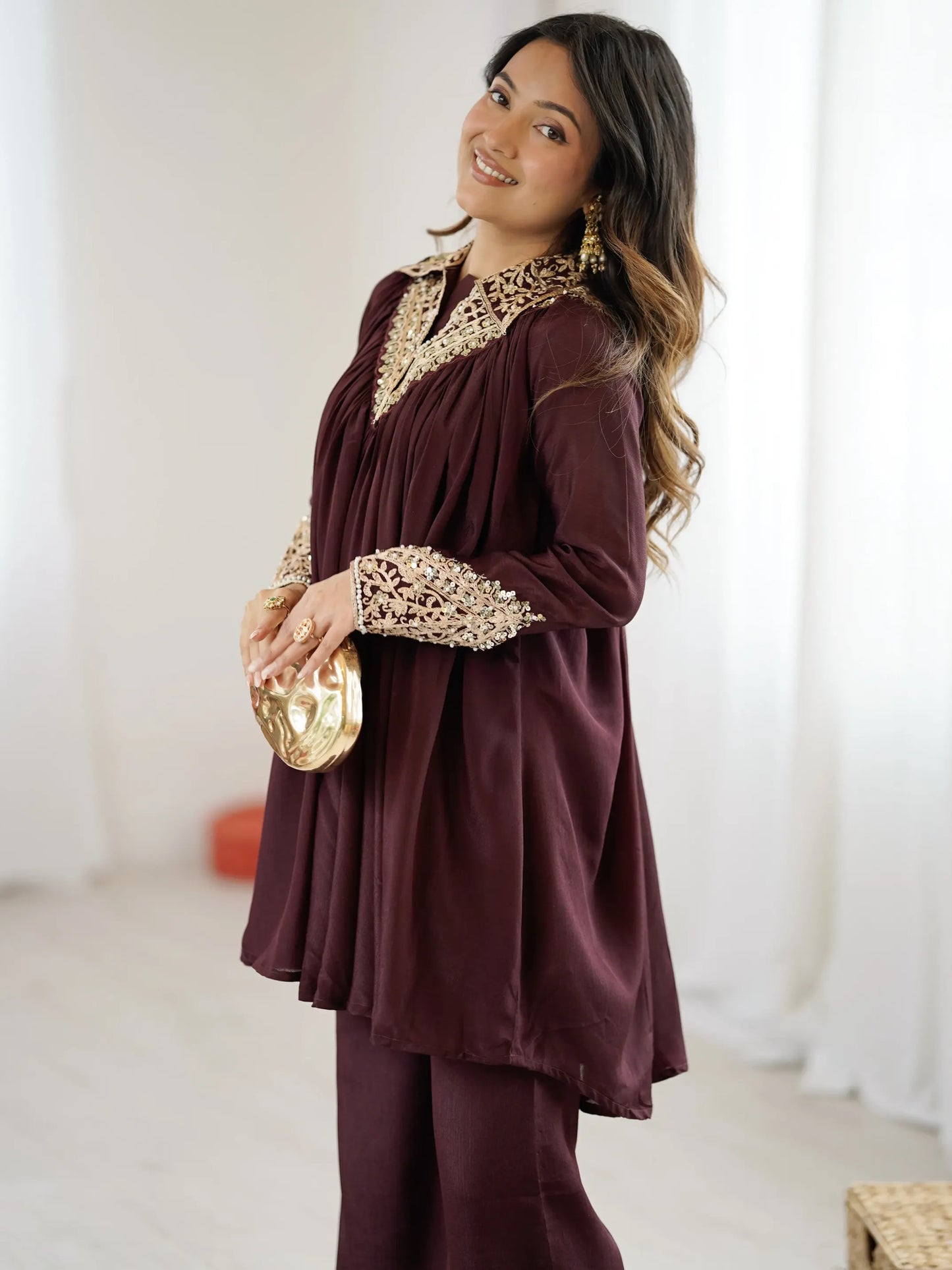 Woman wearing a burgundy outfit with gold embroidery in a bright room.