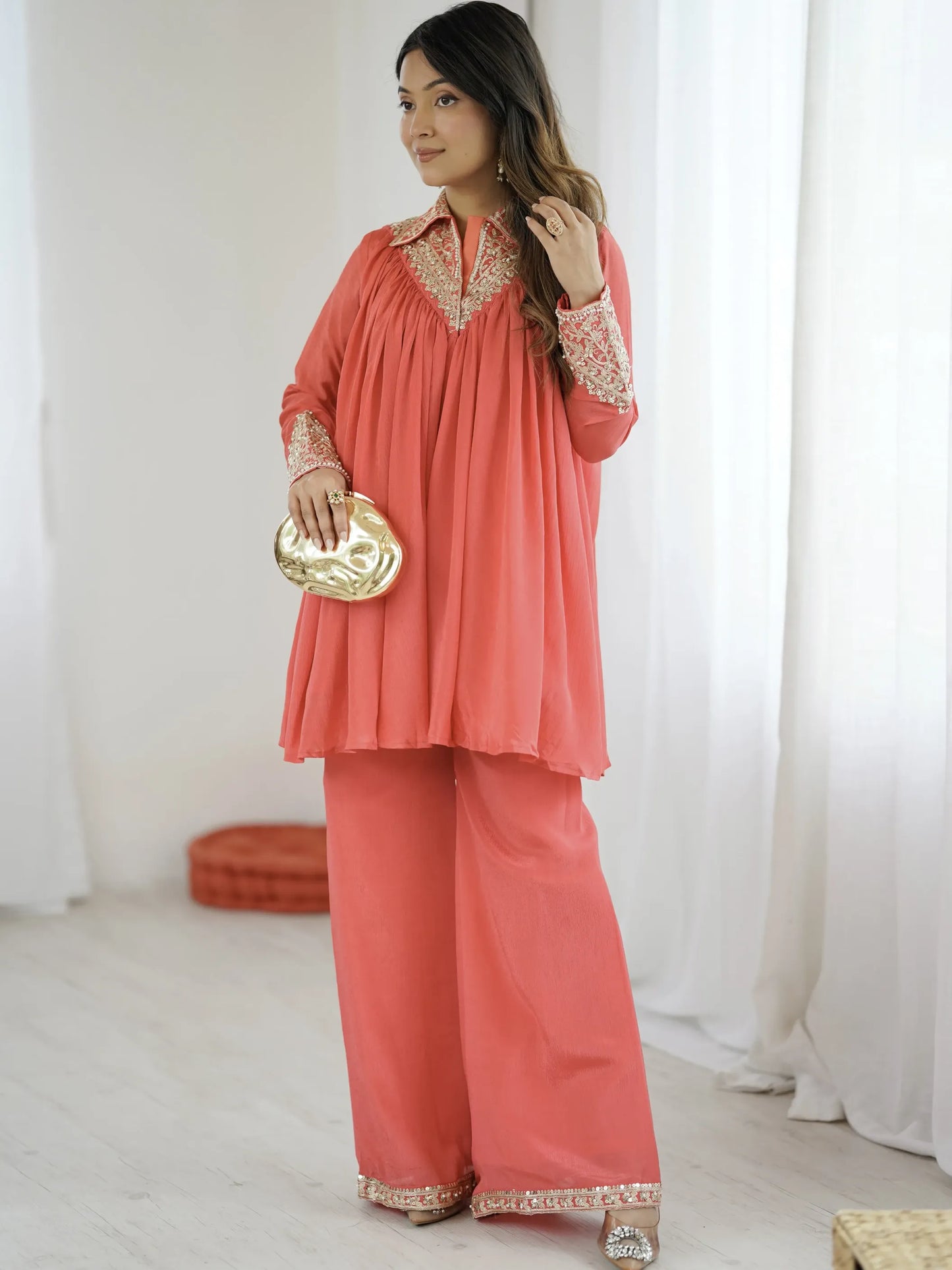 Woman wearing a coral outfit with gold details in a bright room.