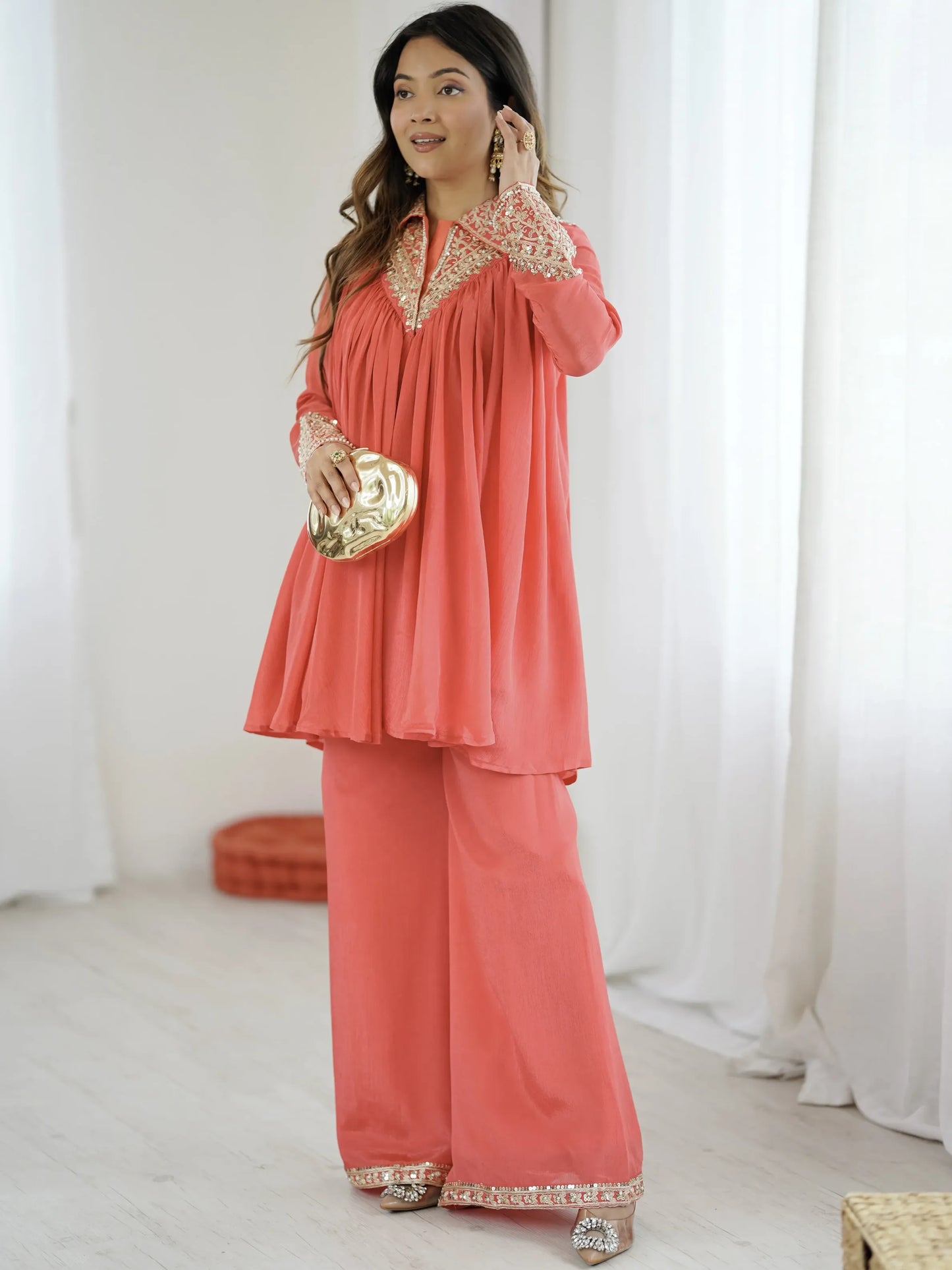 Woman wearing a coral outfit with gold details in a white room.