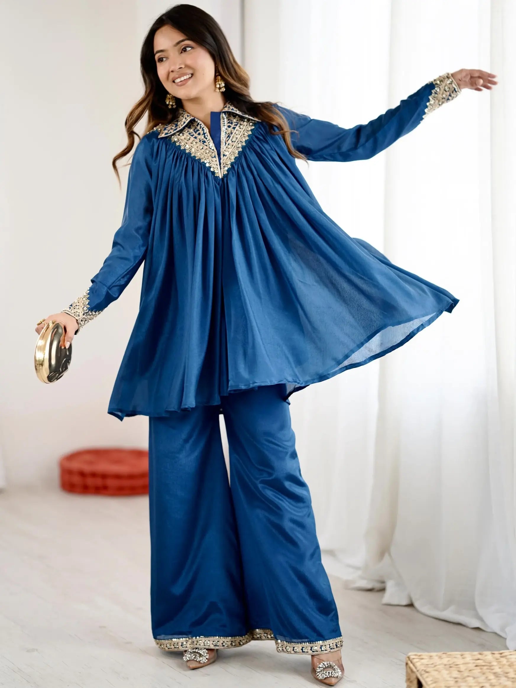 Woman wearing a blue traditional outfit with gold embroidery in a bright room.