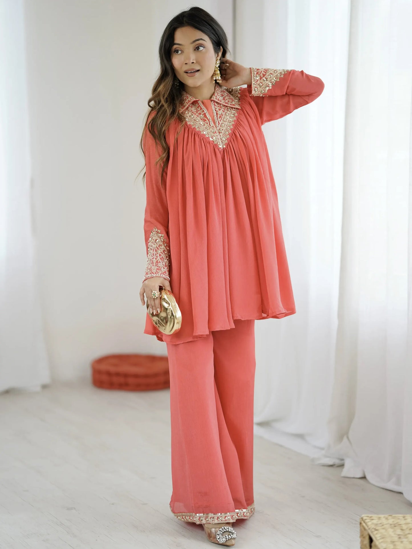 Woman wearing a coral outfit with gold accents in a bright room.