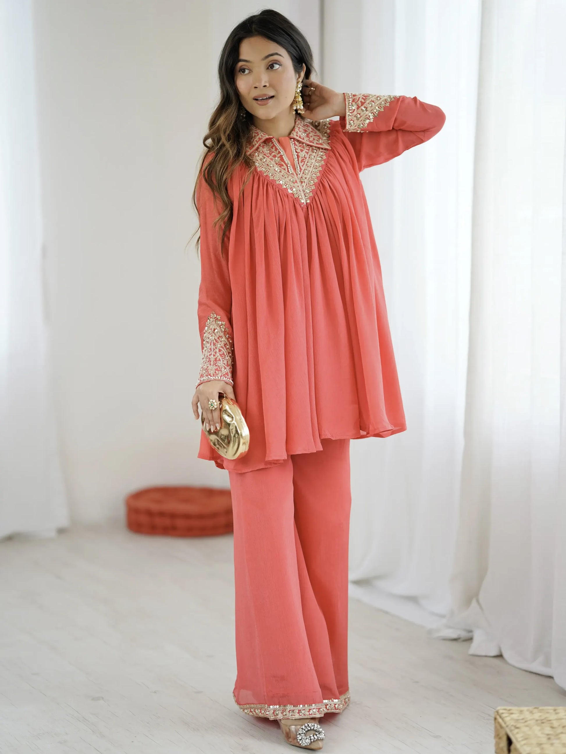 Woman wearing a coral outfit with gold accents in a bright room.