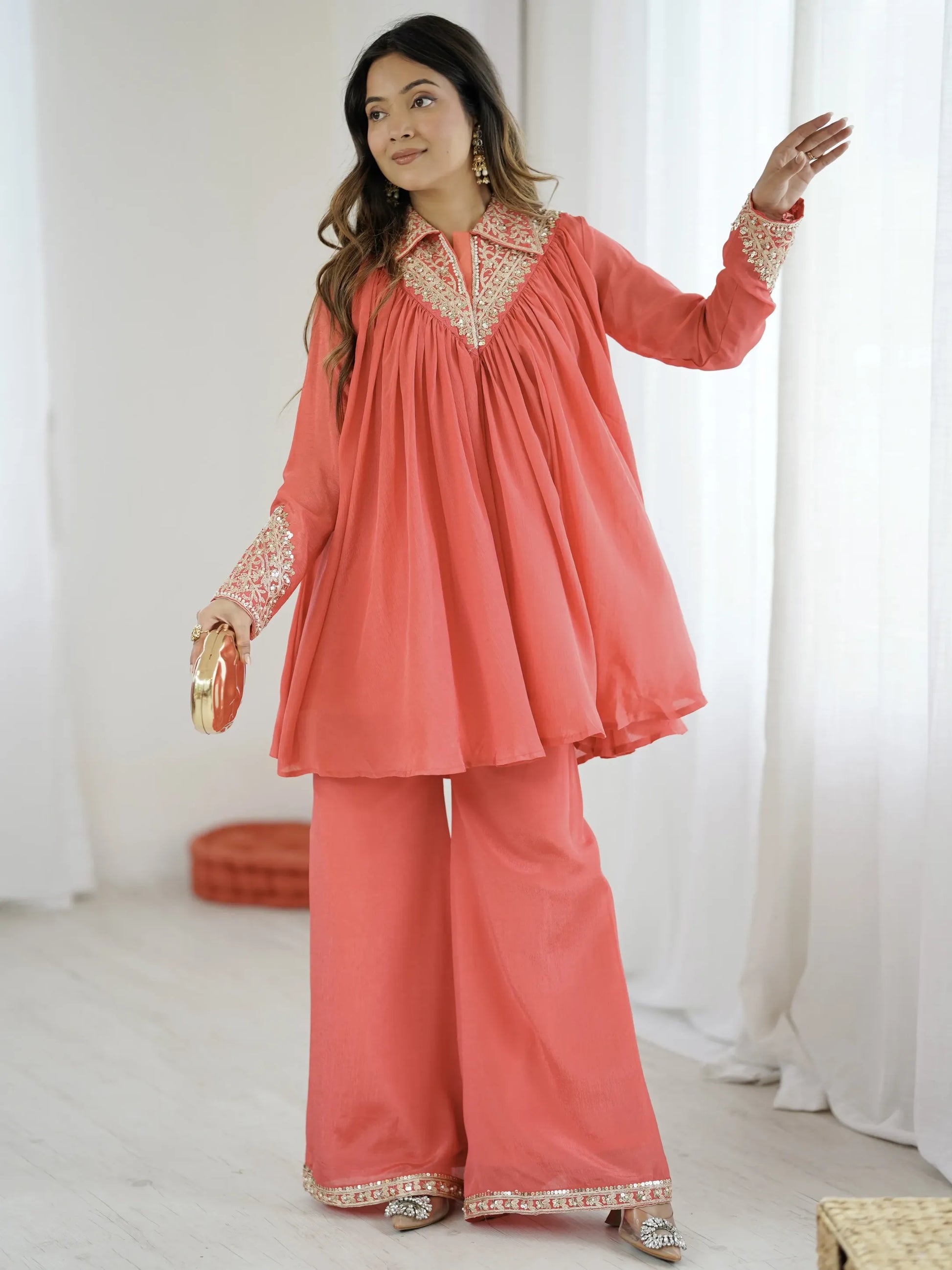 Woman wearing a coral traditional outfit with white embroidery indoors.