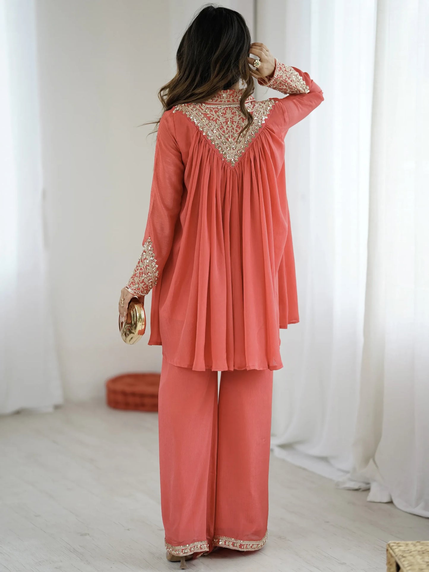 Woman wearing a coral outfit with intricate patterns in a minimalistic setting