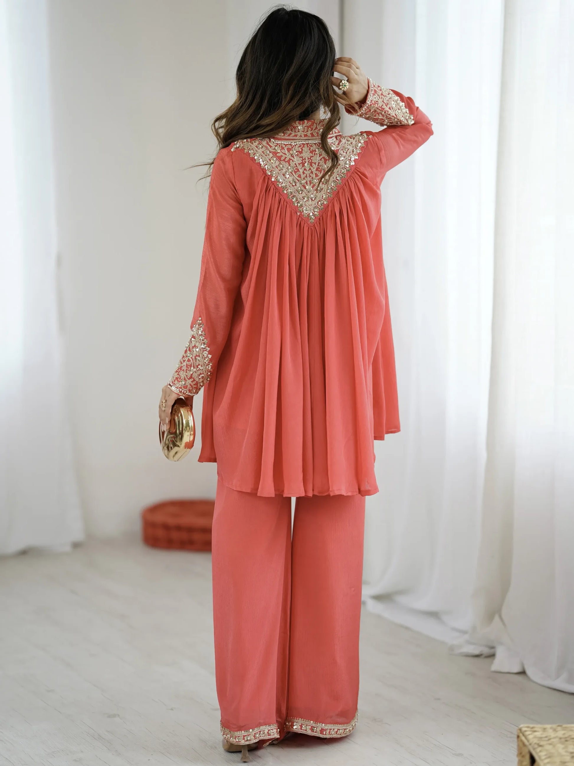 Woman wearing a coral outfit with intricate patterns in a minimalistic setting