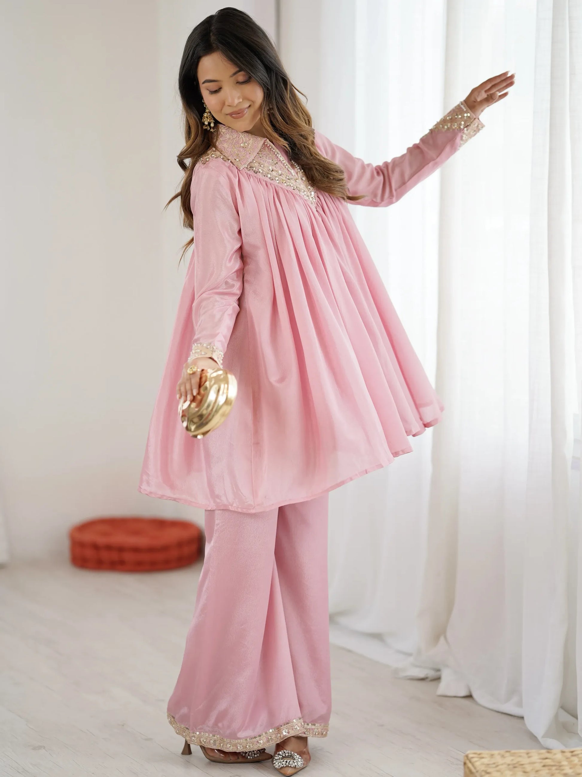Woman wearing a pink traditional outfit with gold details in a bright room.