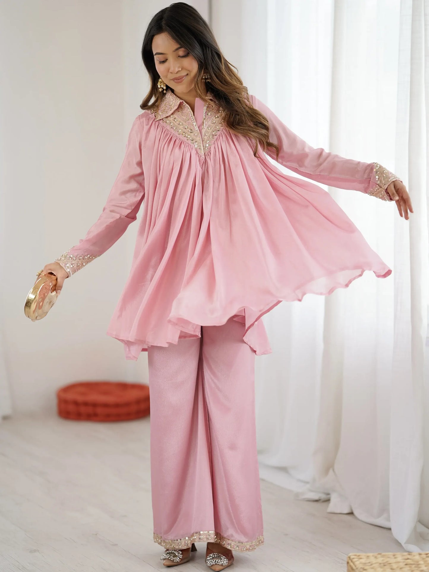 Woman wearing a pink traditional outfit with gold accents in a bright room.