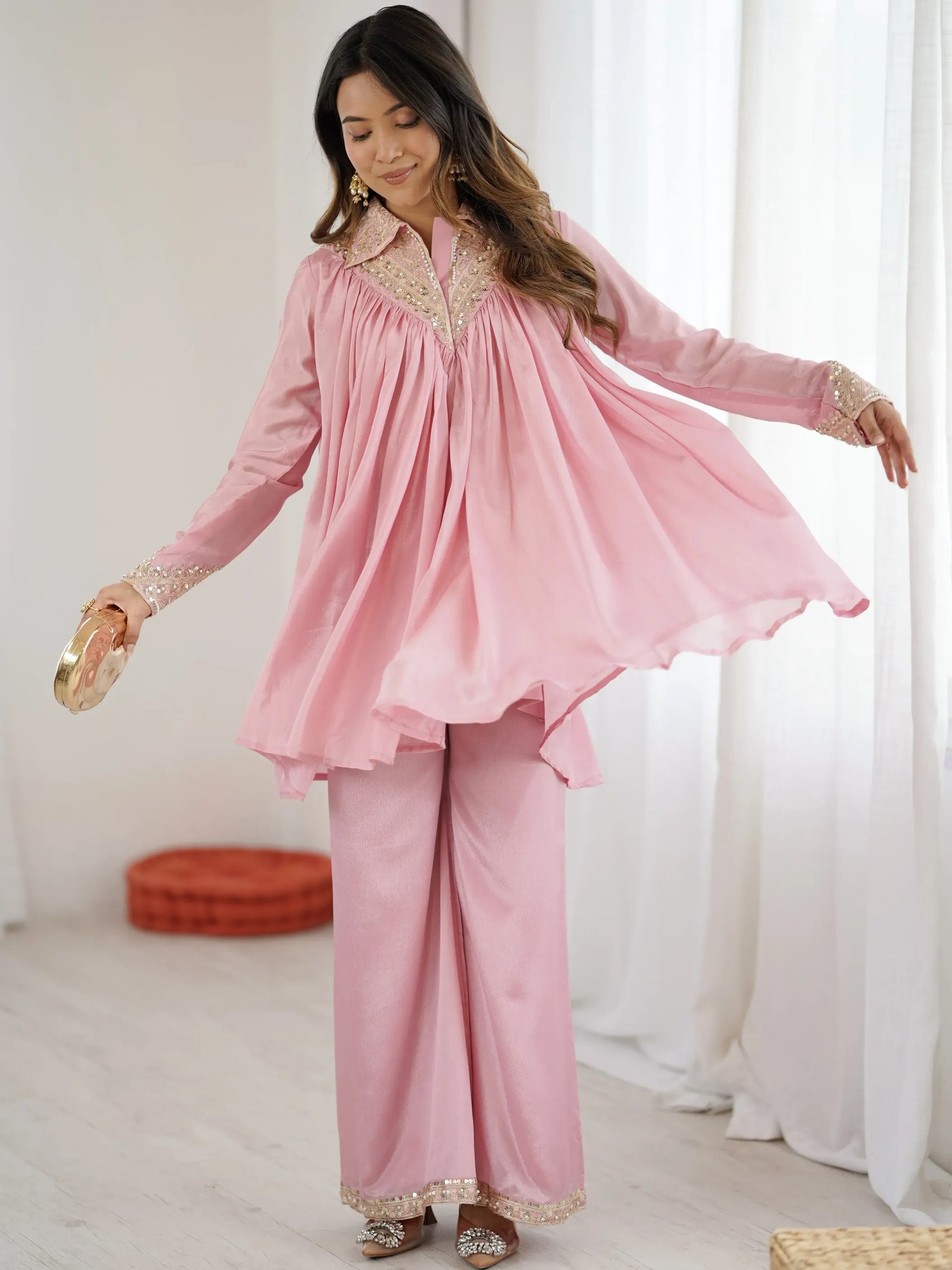 Woman wearing a pink traditional outfit with gold accents in a bright room.