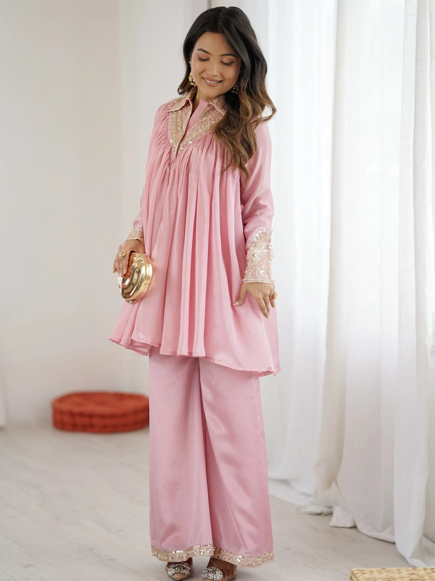 Woman wearing a pink traditional outfit with gold details in a bright room.