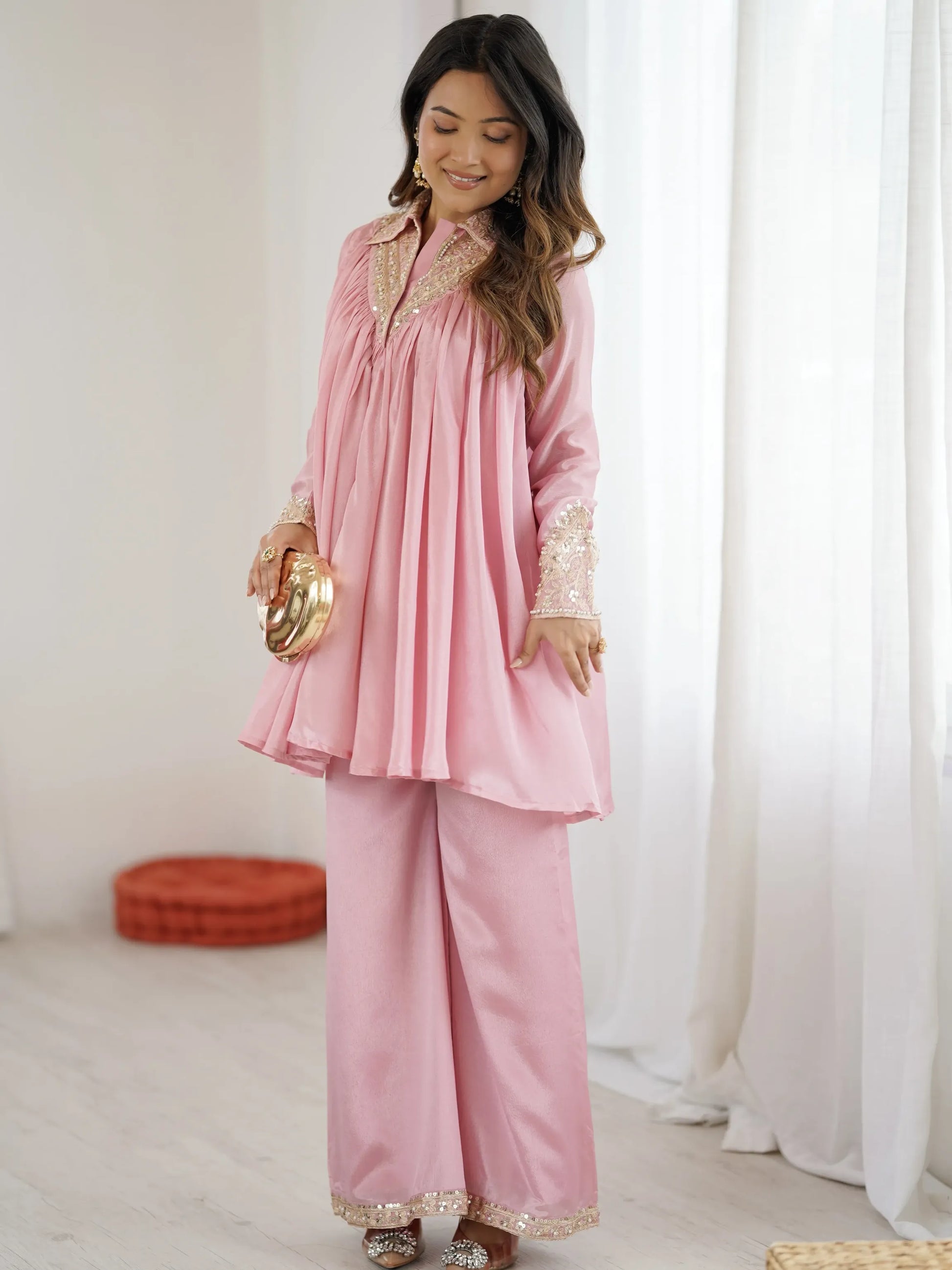Woman wearing a pink traditional outfit with gold details in a bright room.