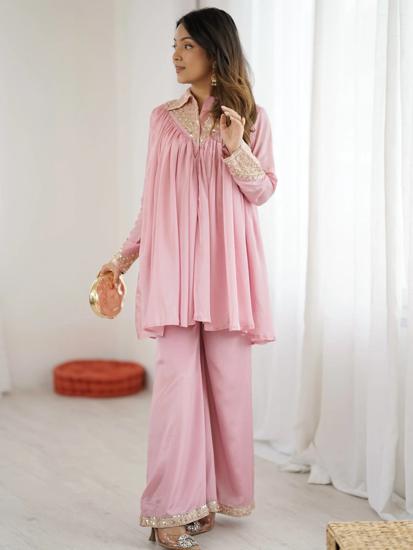 Woman wearing a pink traditional outfit with gold embroidery in a minimalistic setting.