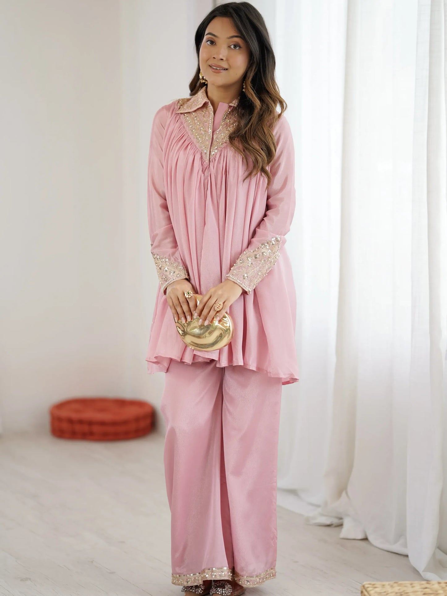 Woman wearing a pink traditional outfit with gold accents in a bright room.