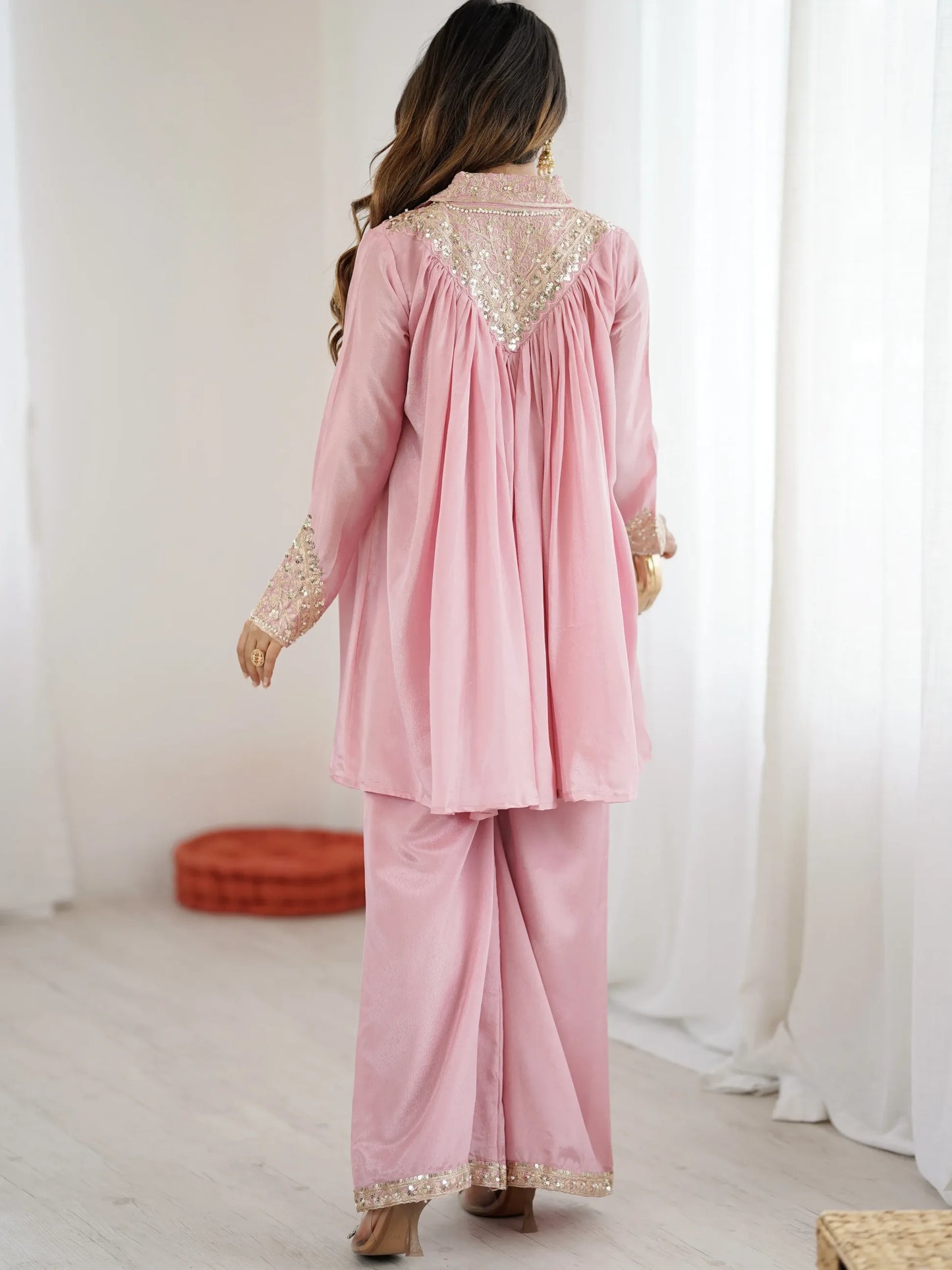 Woman wearing a pink traditional outfit with gold embroidery in a minimalistic setting.