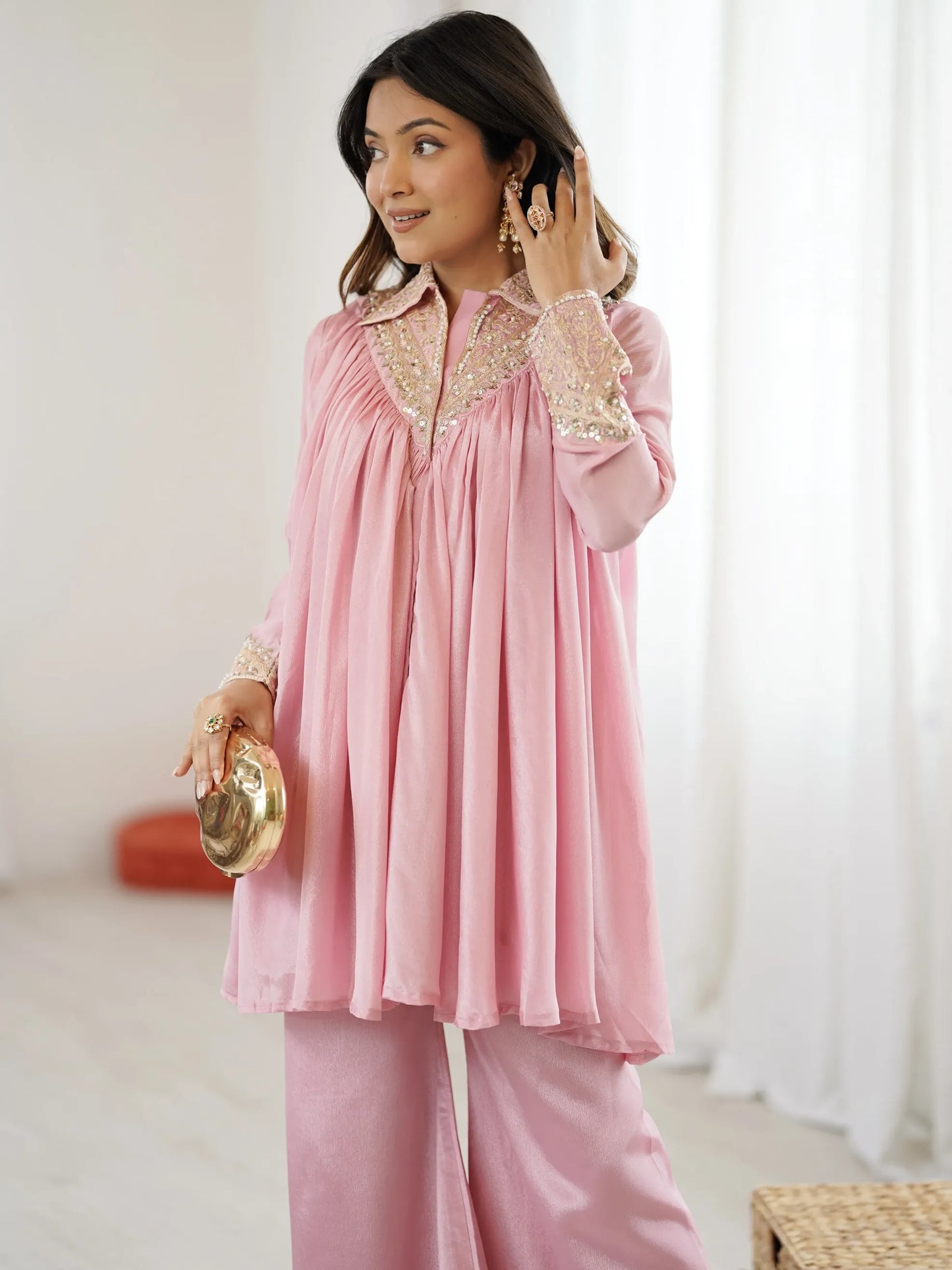 Woman wearing a pink traditional outfit with gold embroidery indoors.