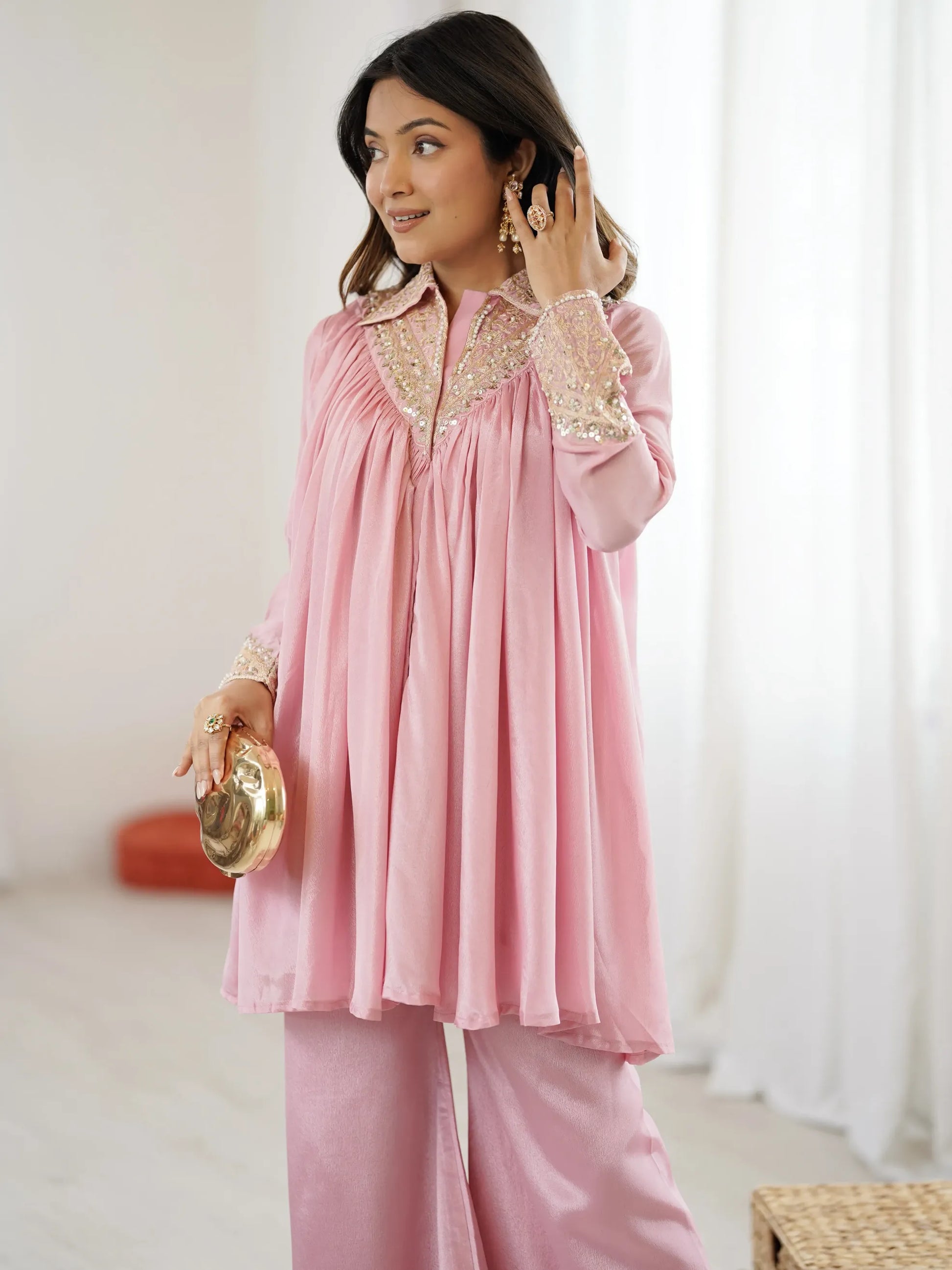 Woman wearing a pink traditional outfit with gold embroidery indoors.