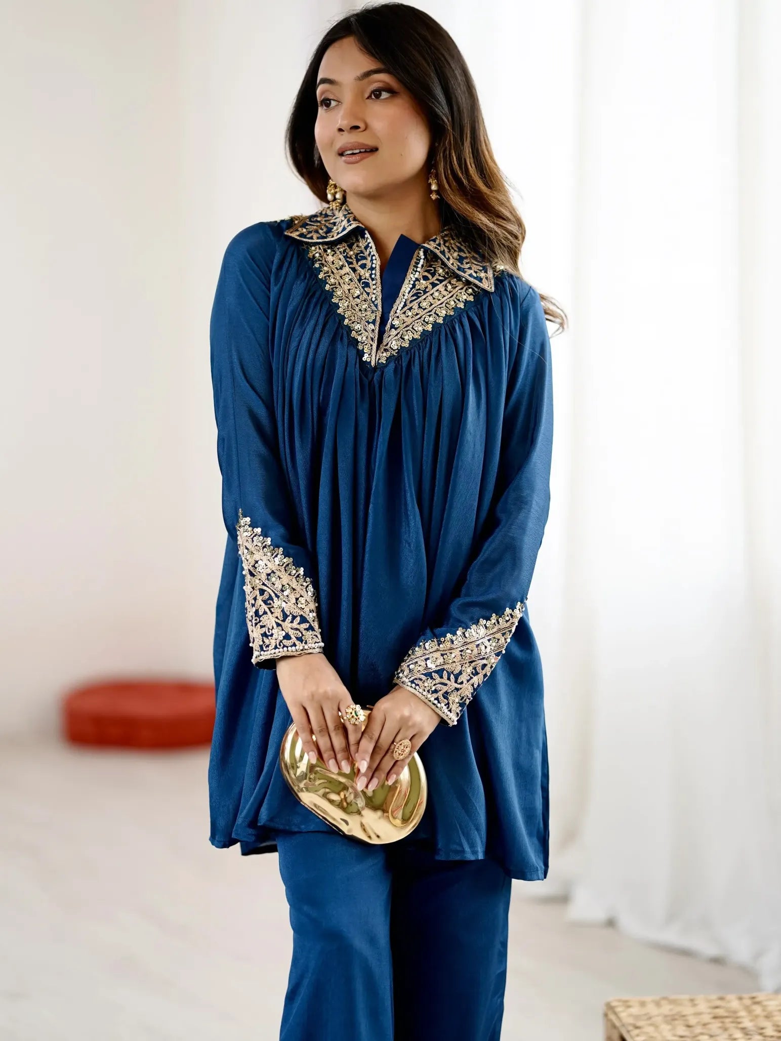 Woman wearing a blue outfit with intricate patterns, holding a gold clutch.