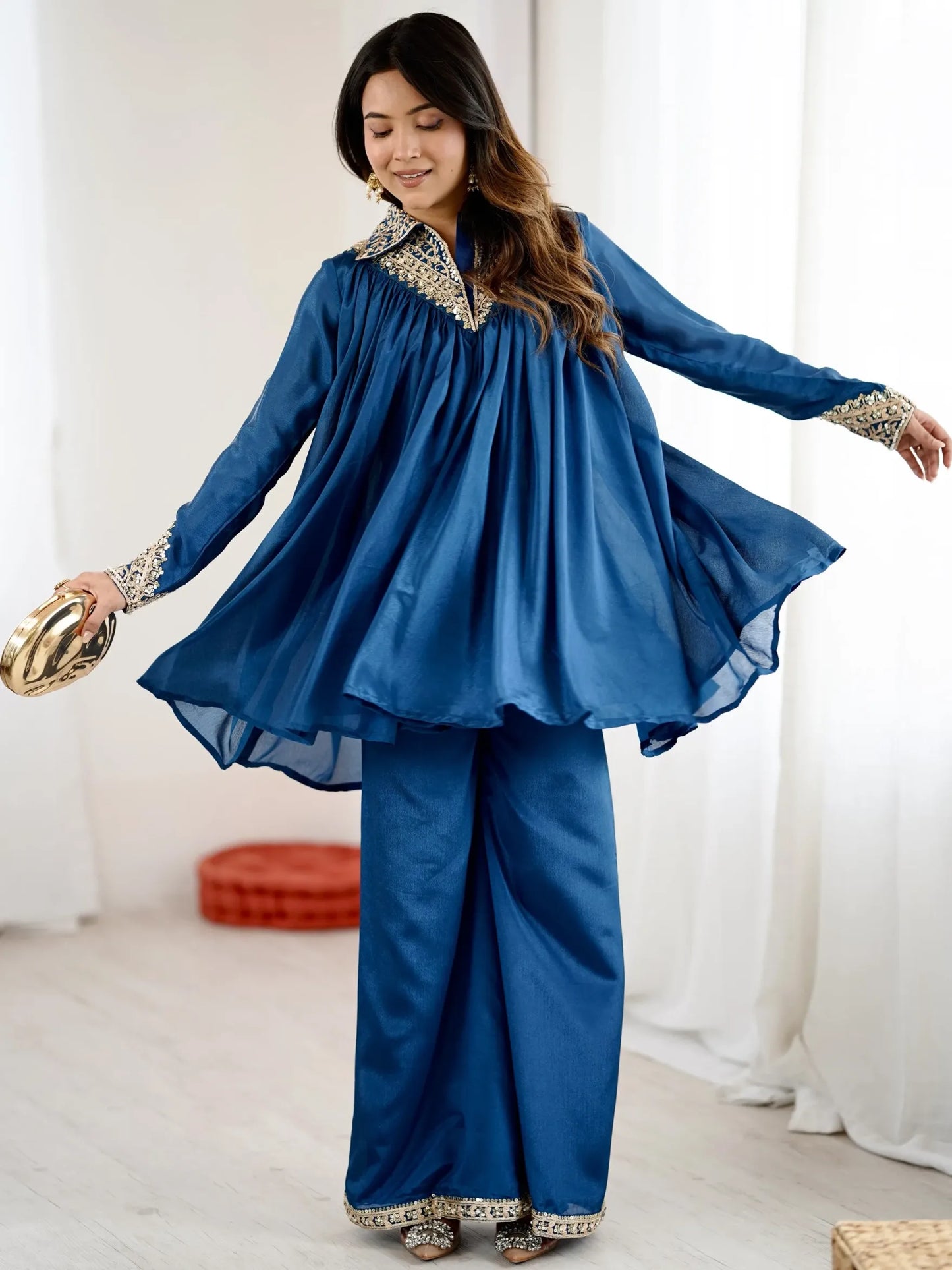 Woman wearing a blue traditional outfit with gold details in a bright room.