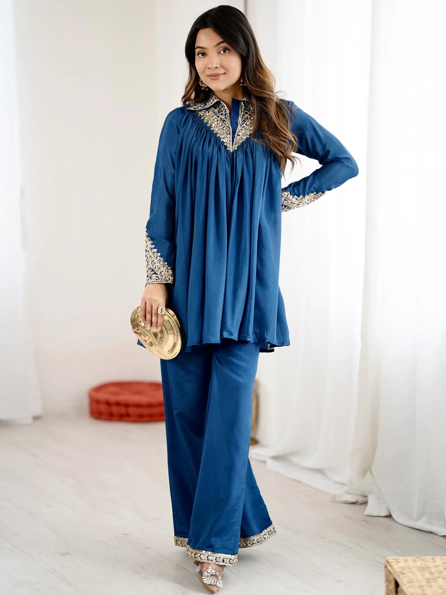 Woman wearing a blue traditional outfit with white embroidery in a bright room.