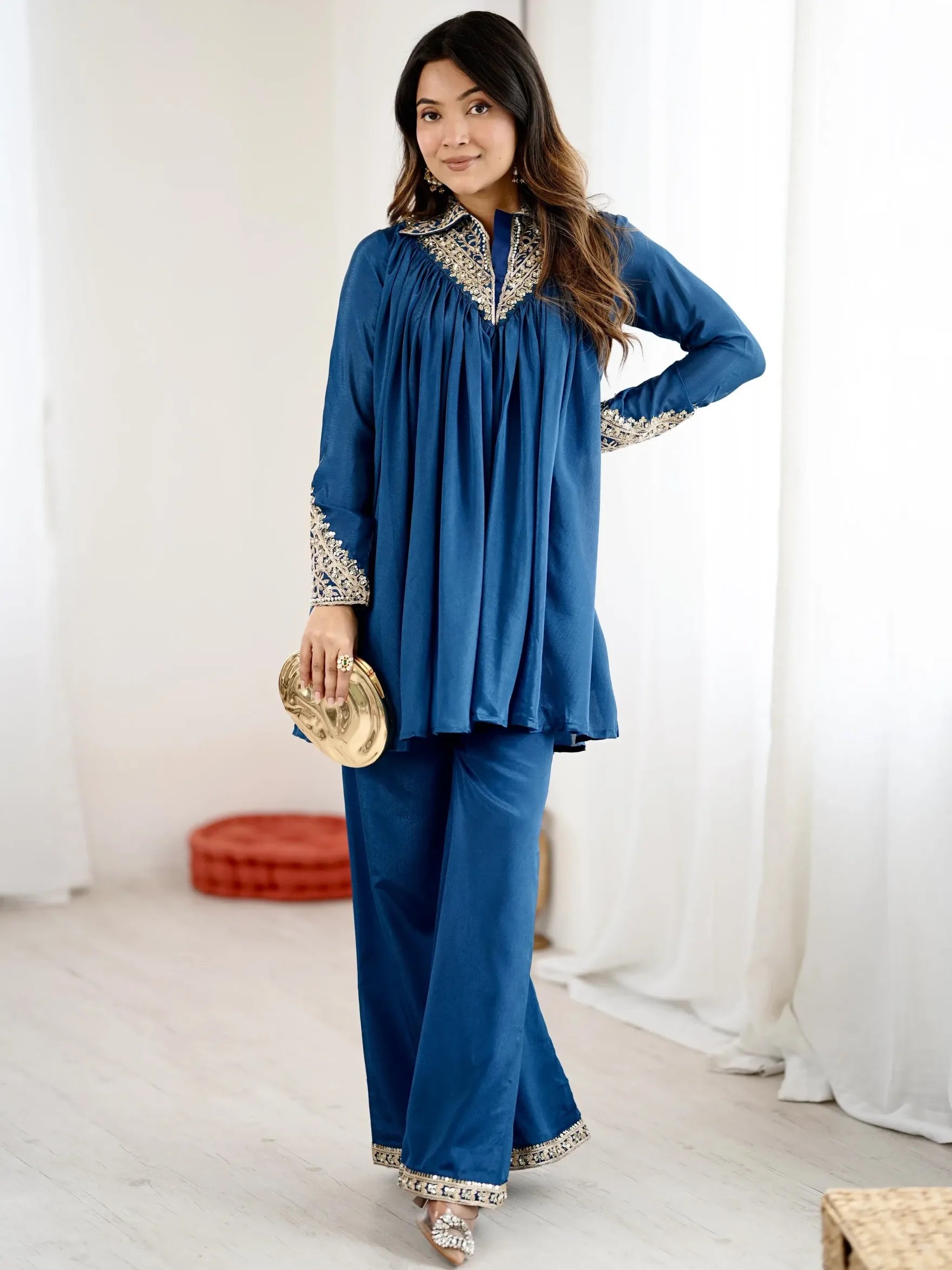 Woman wearing a blue traditional outfit with white embroidery in a bright room.