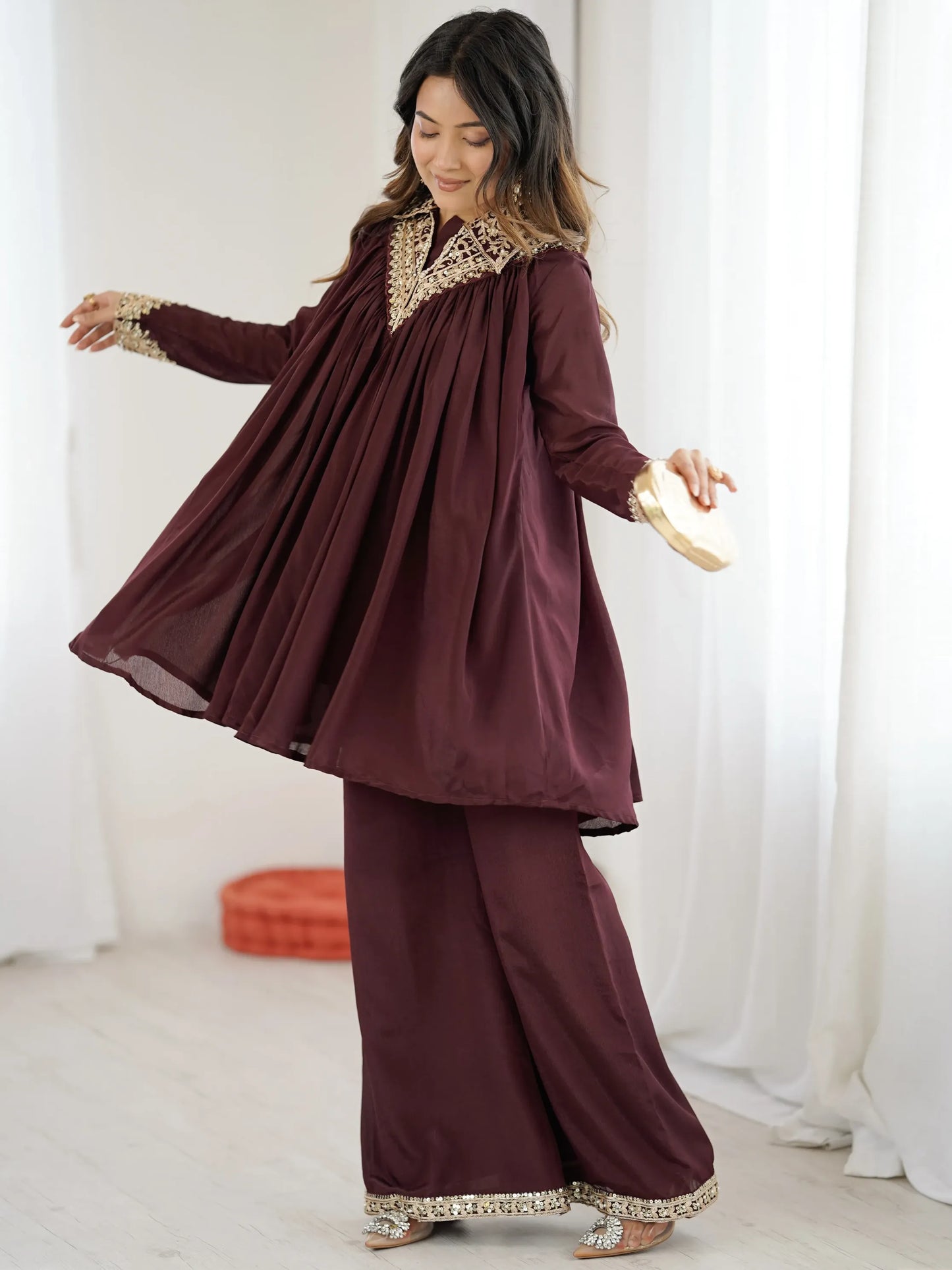 Woman wearing a burgundy traditional outfit with gold embroidery against a white curtain background