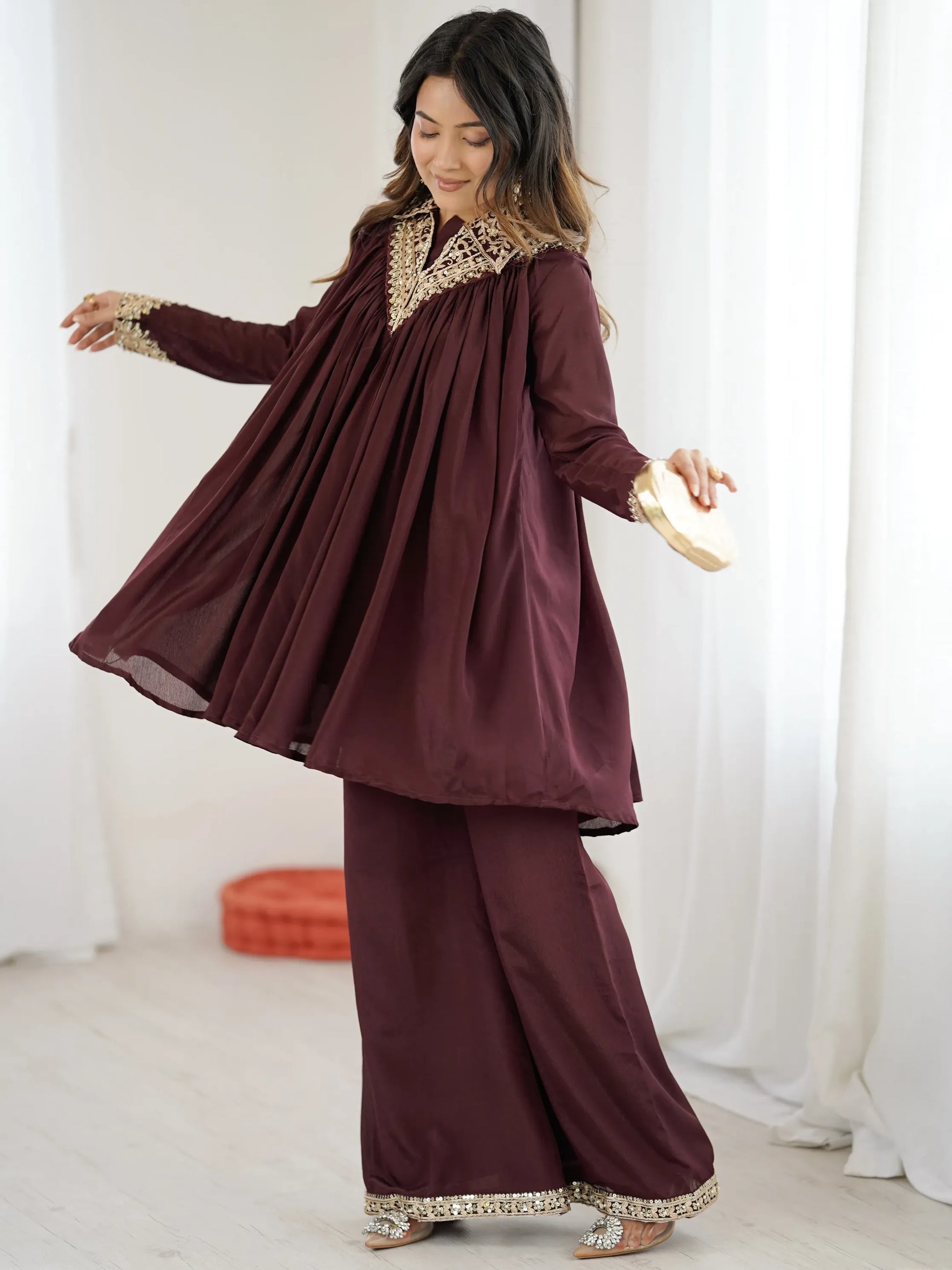Woman wearing a burgundy traditional outfit with gold embroidery against a white curtain background