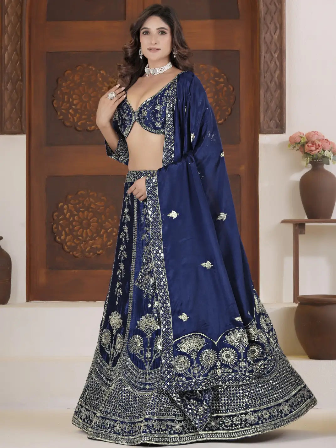 Woman wearing a blue embroidered traditional outfit in a decorated room.
