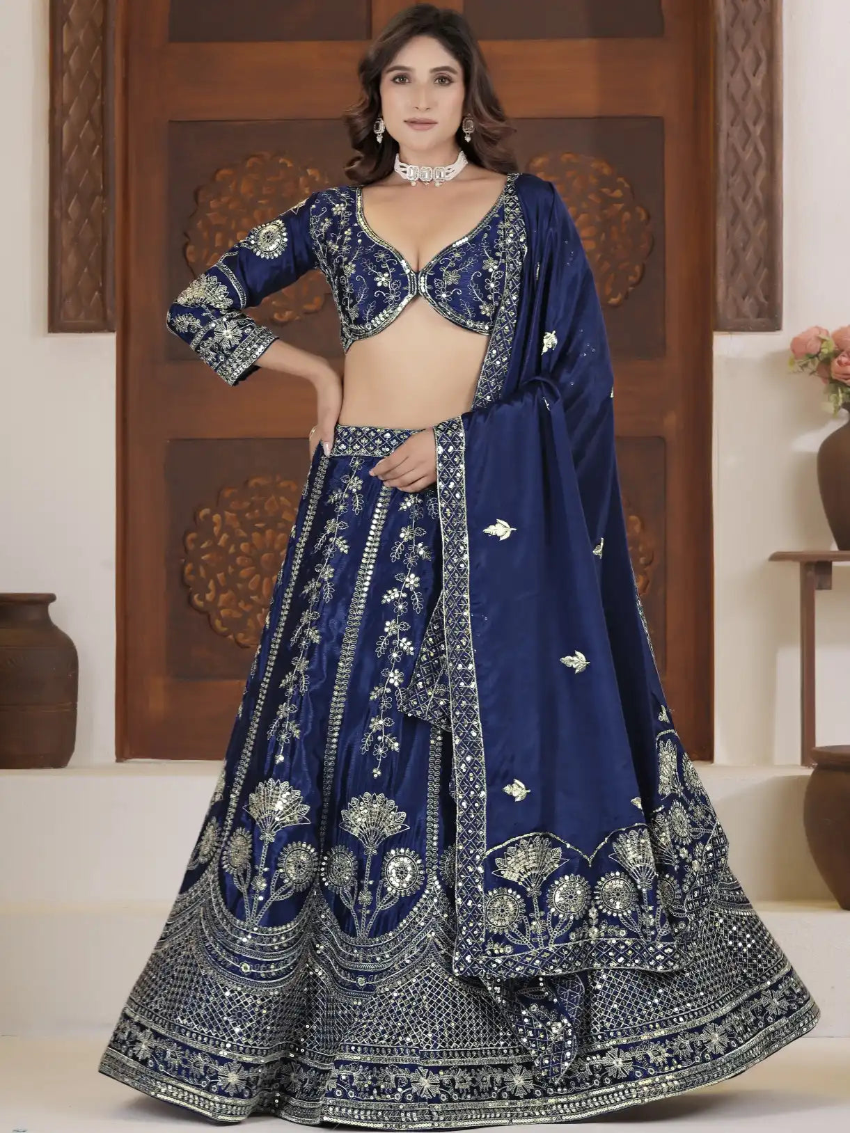 Woman wearing a traditional blue embroidered outfit in a decorated room.