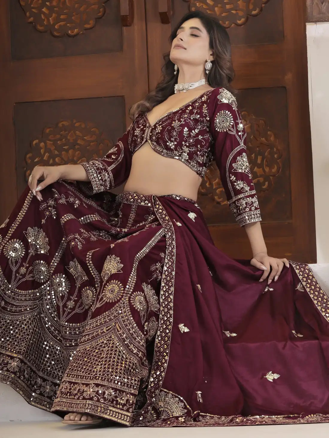 Woman in a maroon embroidered traditional outfit with a decorative background