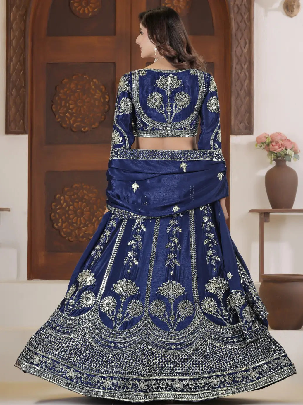 Woman wearing a blue embroidered traditional outfit in a decorated room.