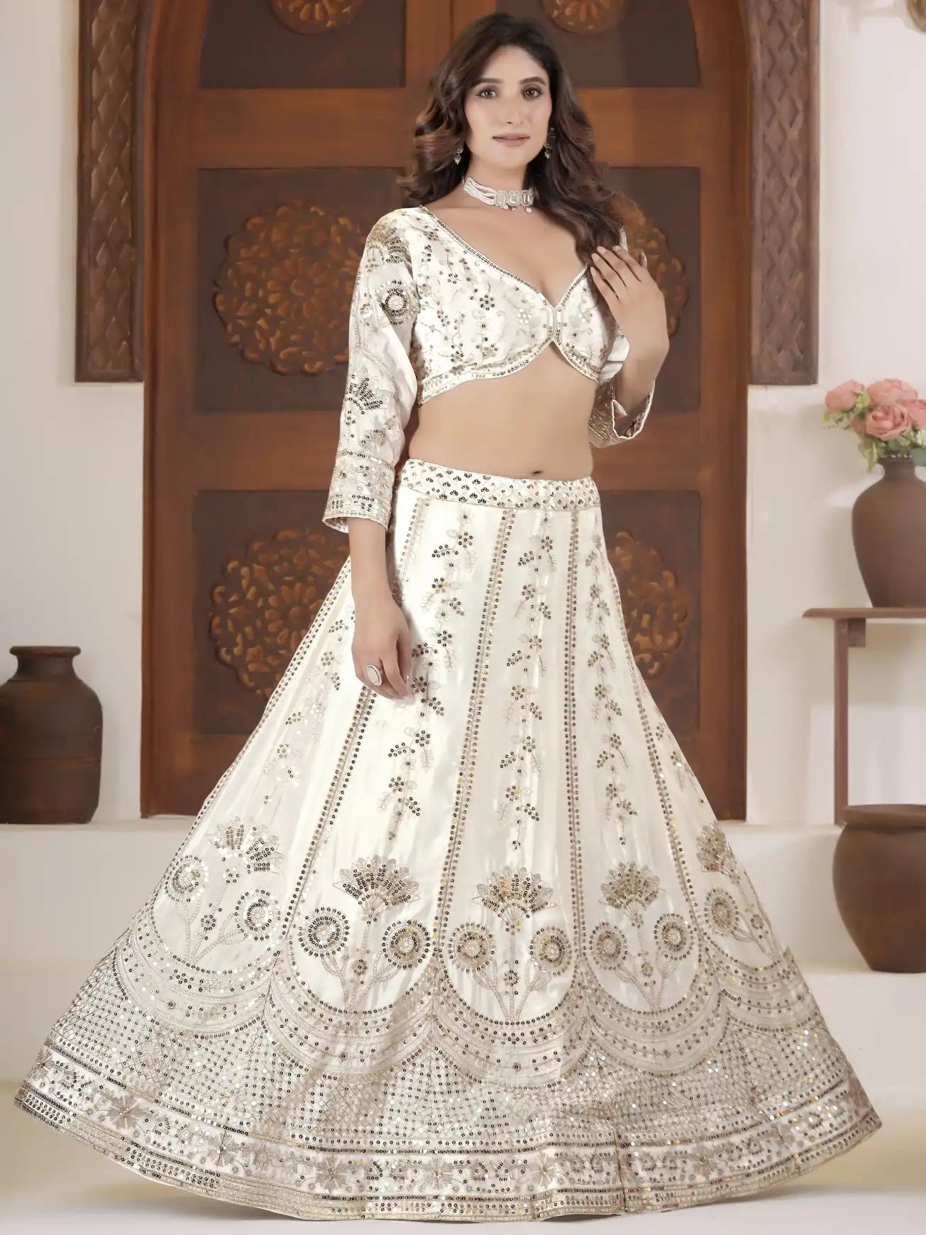 Woman wearing a white embroidered lehenga with a matching blouse in a decorated room.