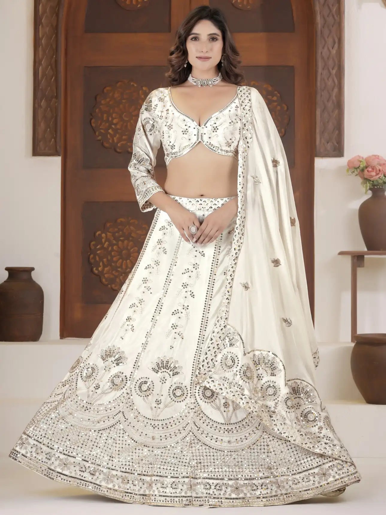 Woman wearing a white embroidered lehenga with a matching blouse in a decorated room.