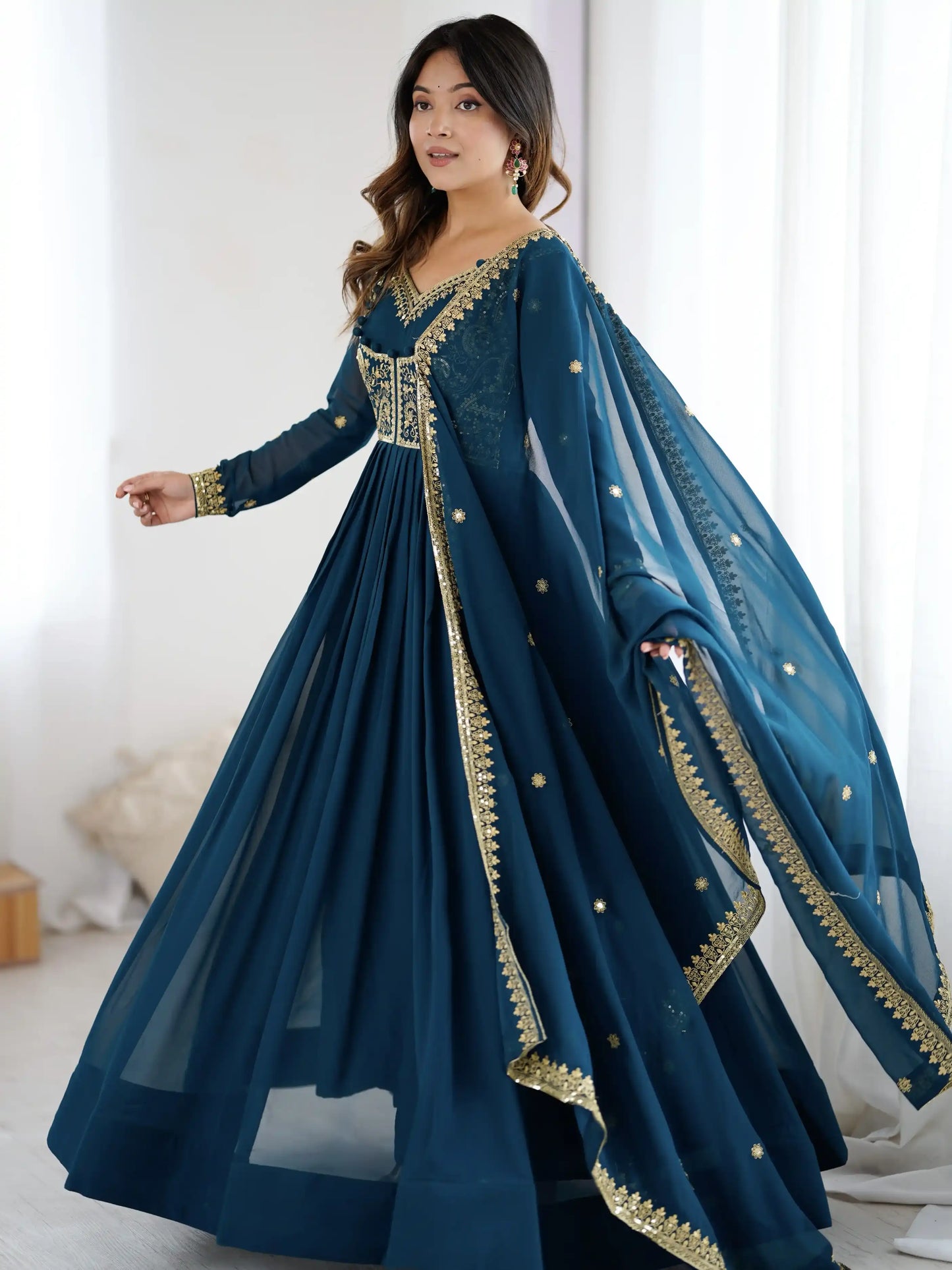Woman wearing a blue traditional outfit with gold embroidery in a bright room.