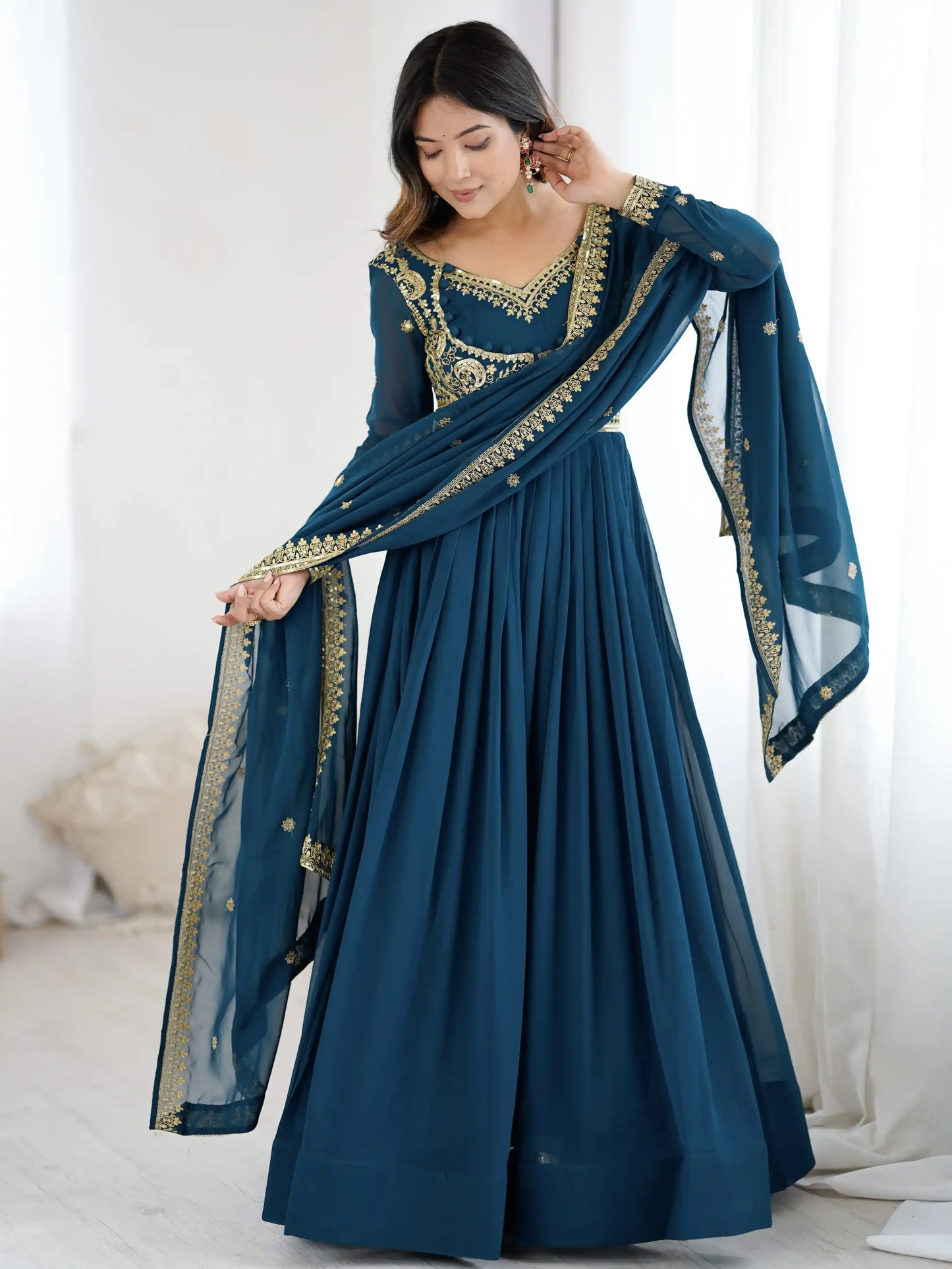 Woman wearing a blue traditional outfit with gold embroidery in a minimalistic setting