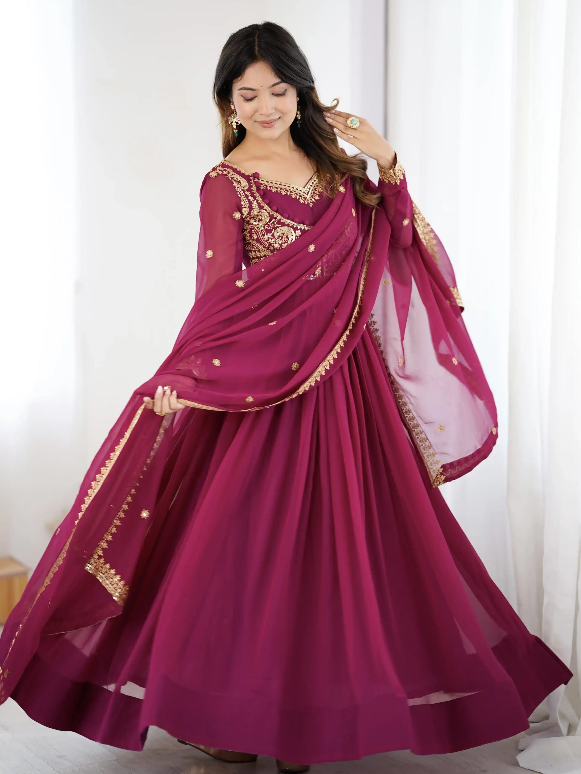 Woman wearing a maroon saree with gold embroidery against a white background