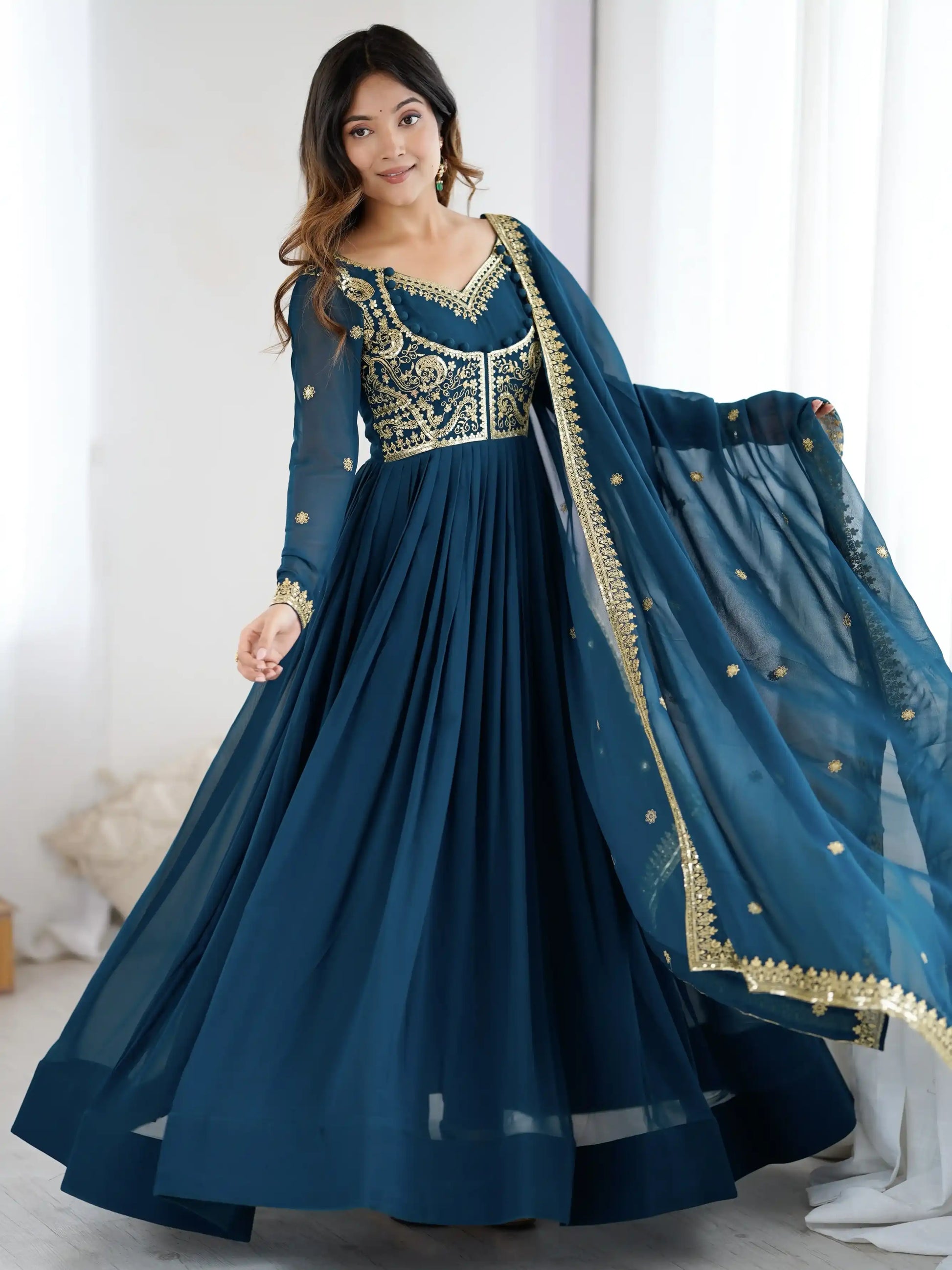 Woman wearing a blue traditional outfit with gold embroidery in a bright room.