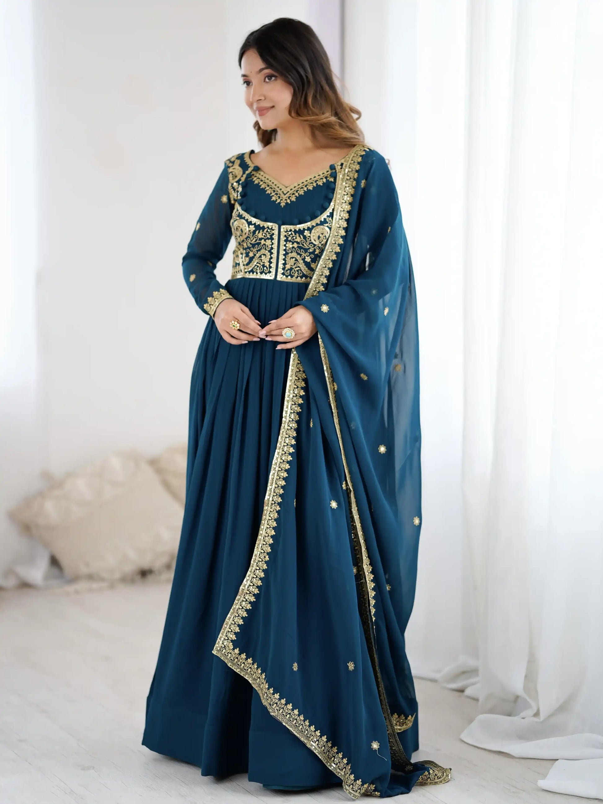 Woman wearing a blue traditional outfit with gold embroidery in a white room.
