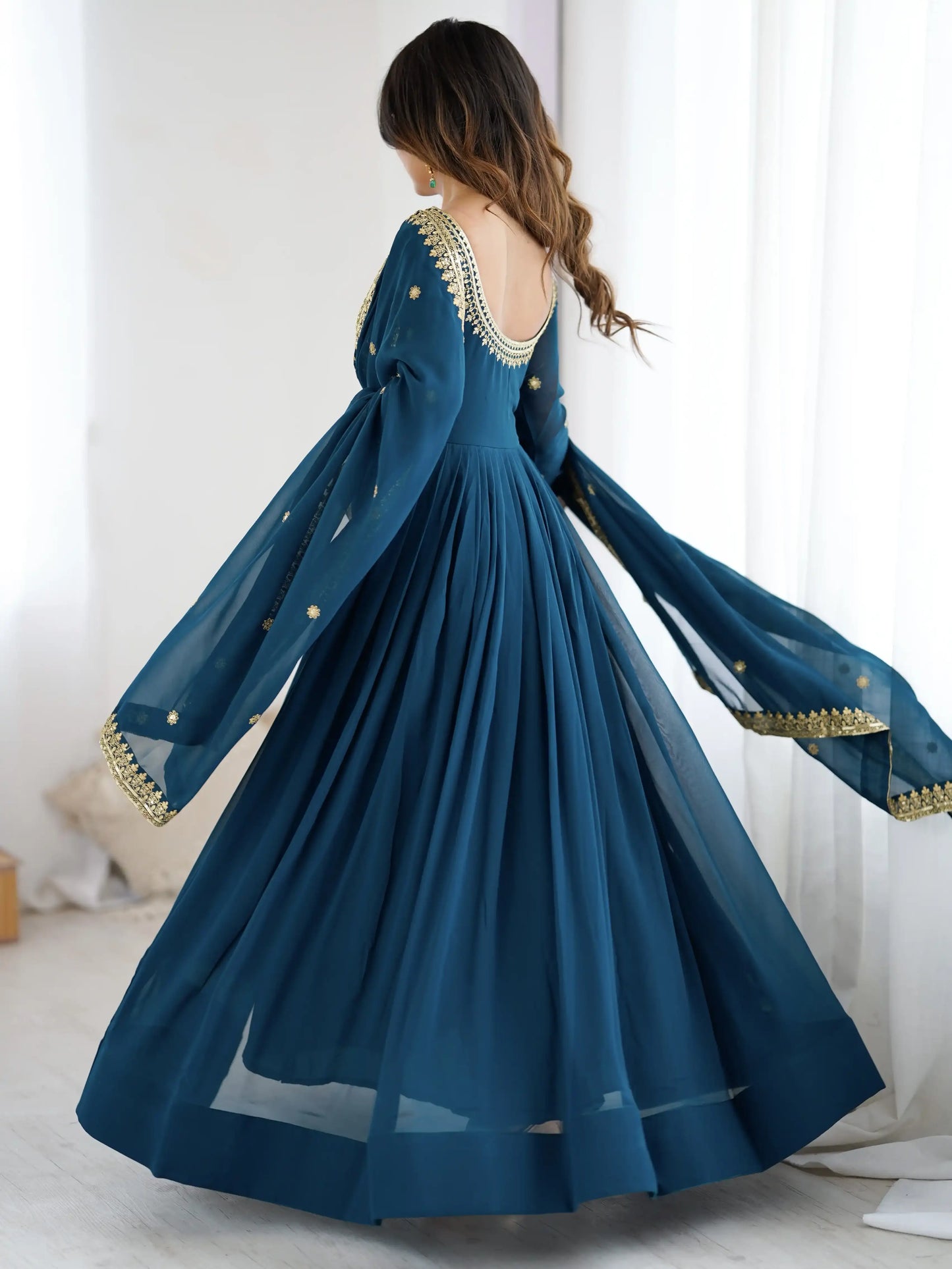 Woman wearing a long blue dress with gold detailing in a bright room.