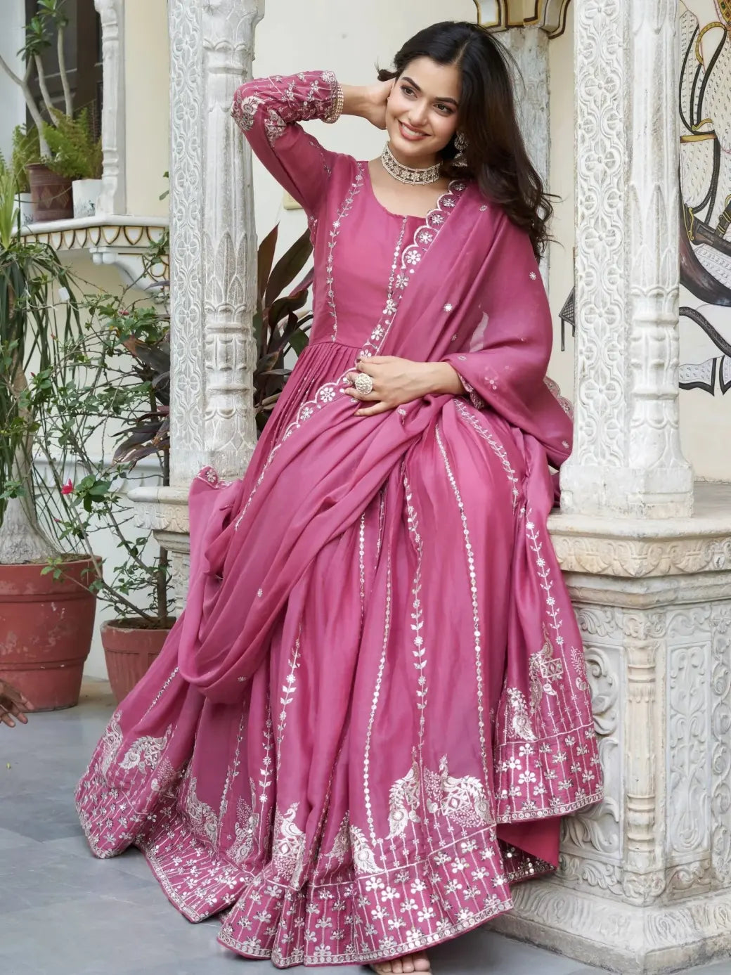 Woman in a pink saree with white patterns sitting on a decorative step.