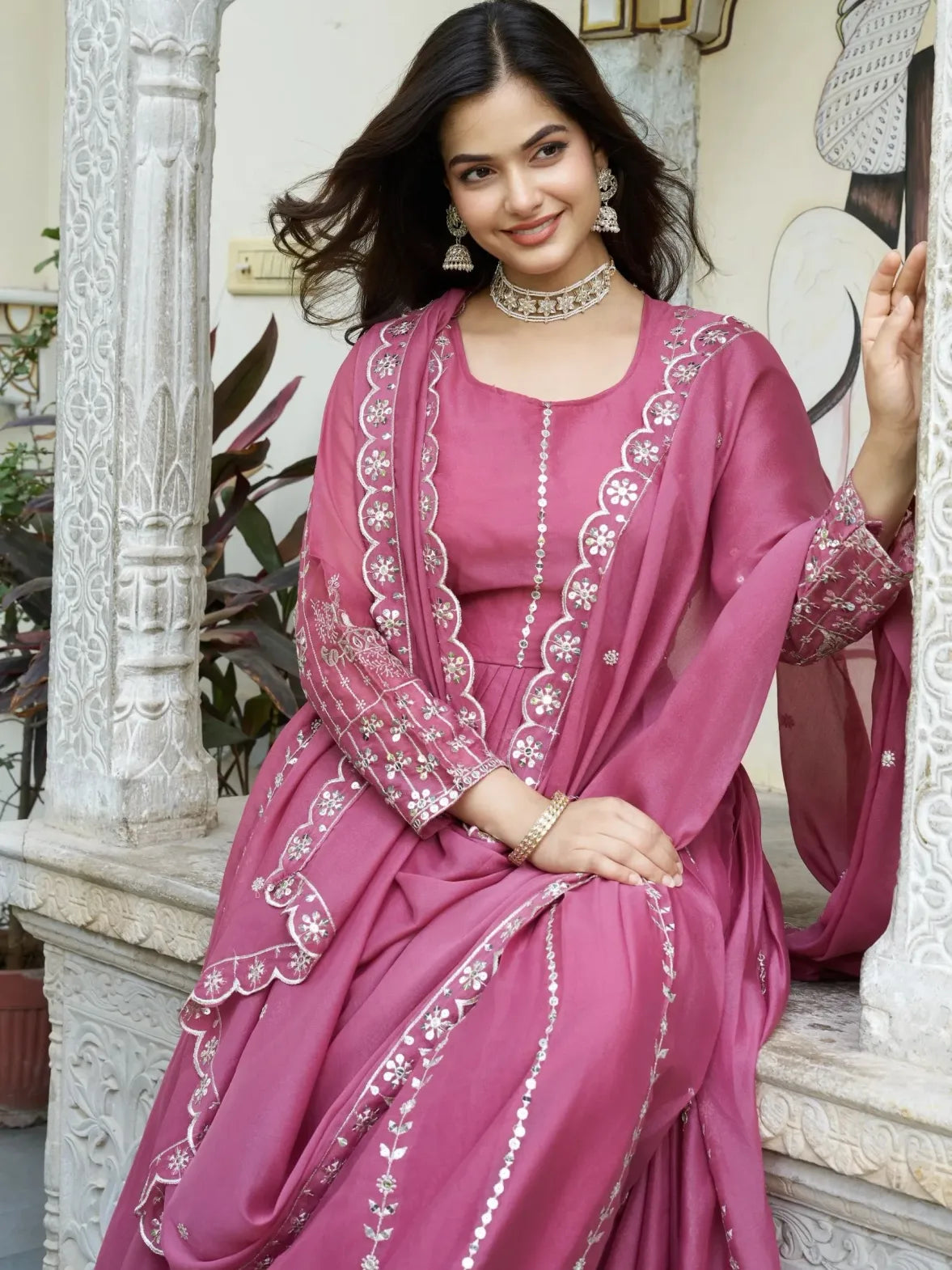 Woman in a pink traditional outfit with white embroidery sitting on steps.